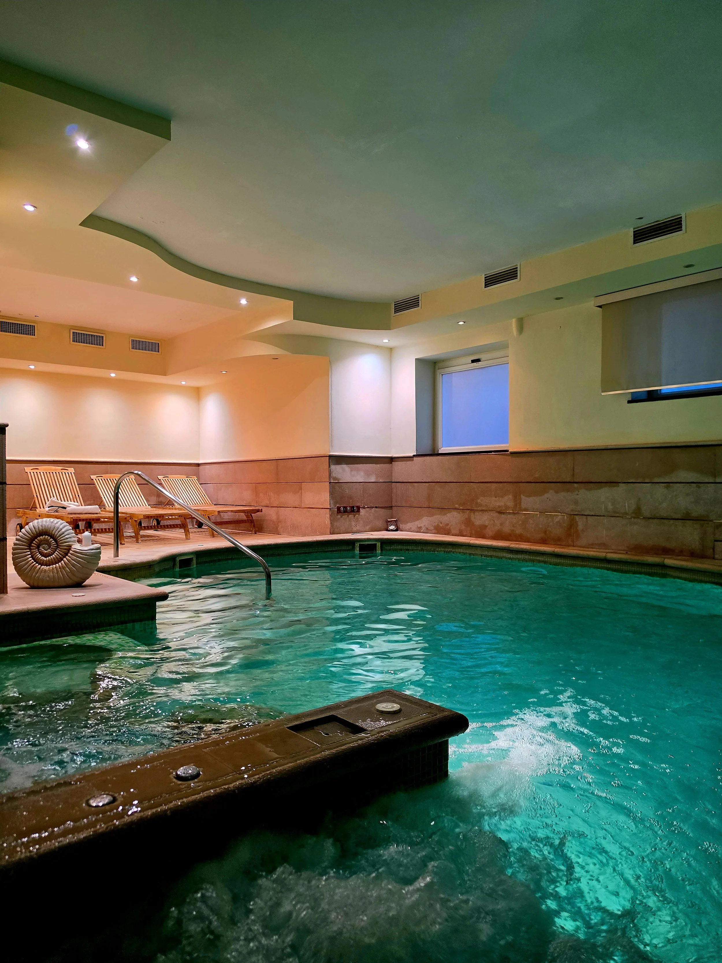 Indoor spa pool with hydrotherapy jets, loungers, and soft ambient lighting