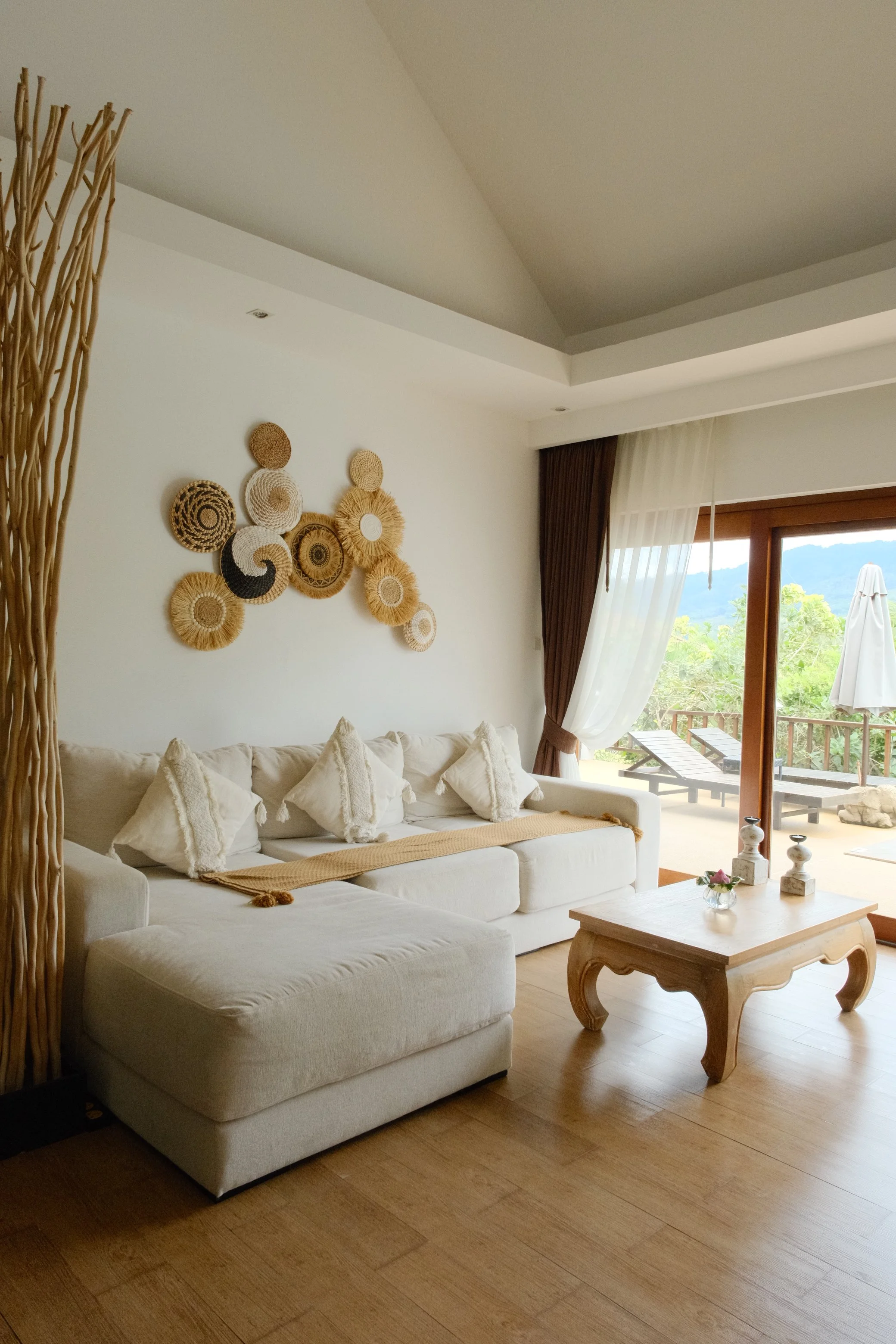 Bright villa living room with neutral furnishings, woven wall art, natural wood, and direct access to a private terrace