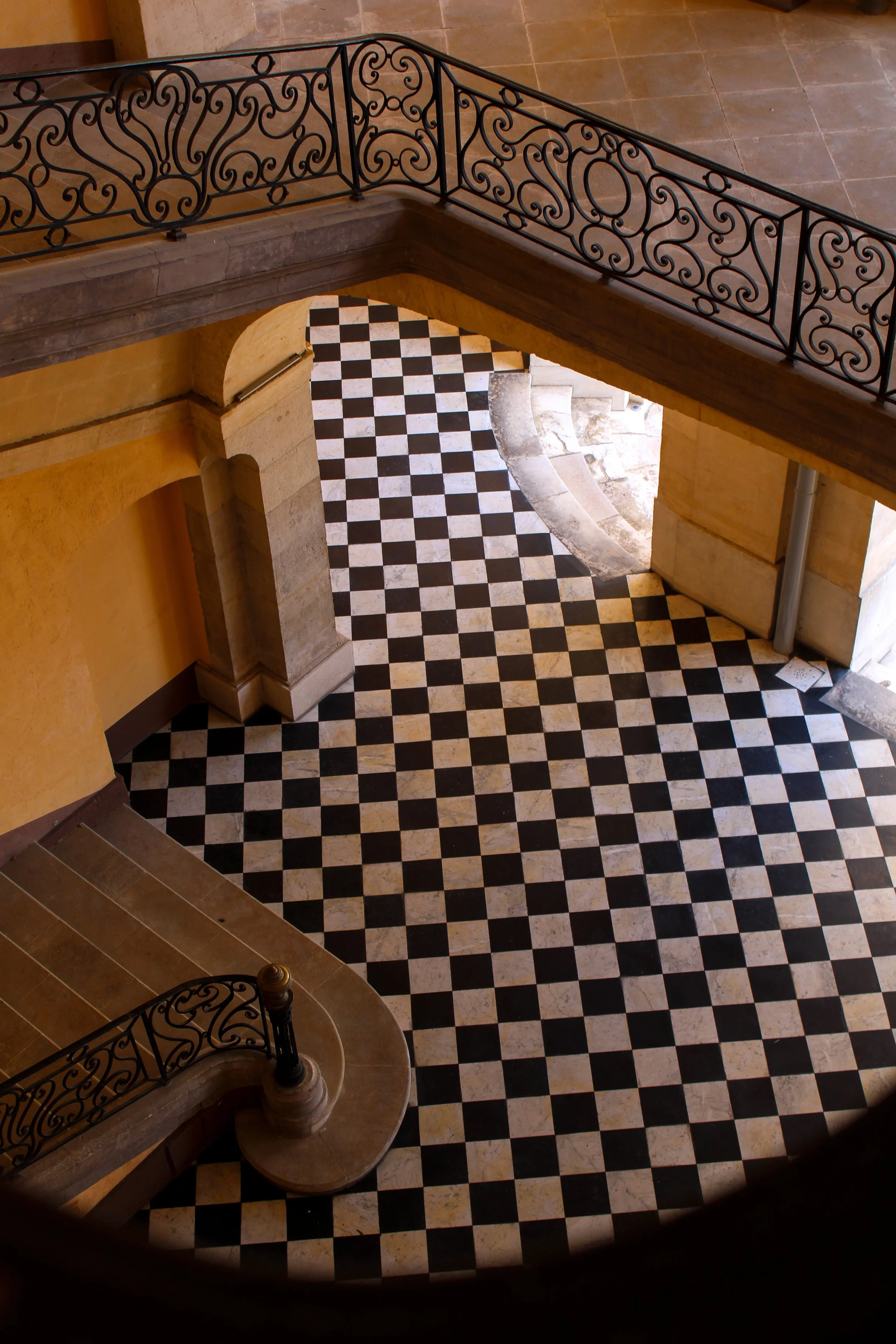 Historic staircase with ornate iron railings and checkerboard marble flooring