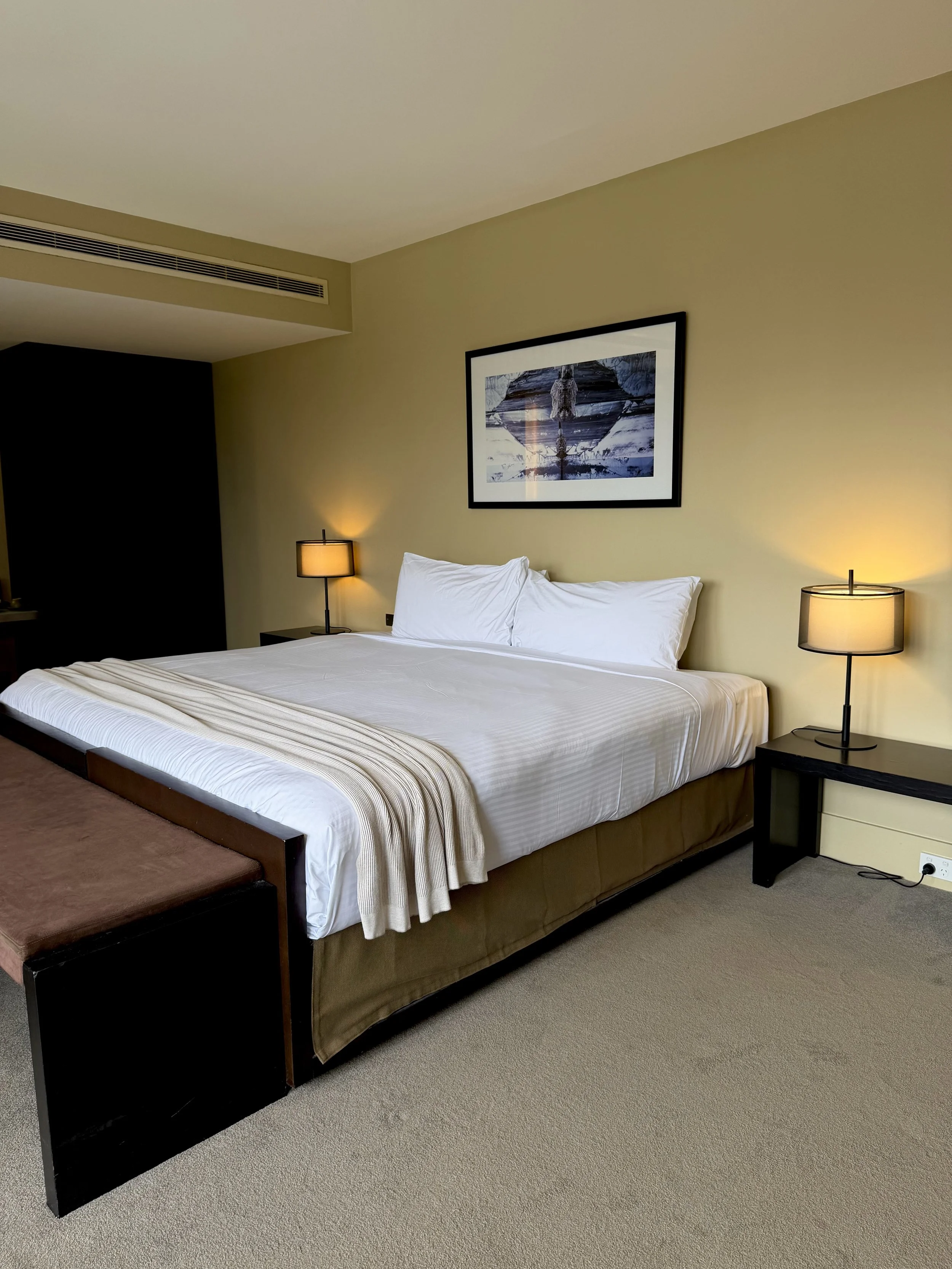 Elegant hotel bedroom featuring a king-size bed, warm bedside lighting, neutral tones, and contemporary furnishings
