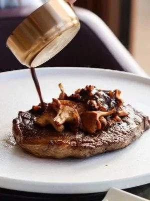 Chef finishing a premium steak with rich sauce at Fingal Hotel restaurant