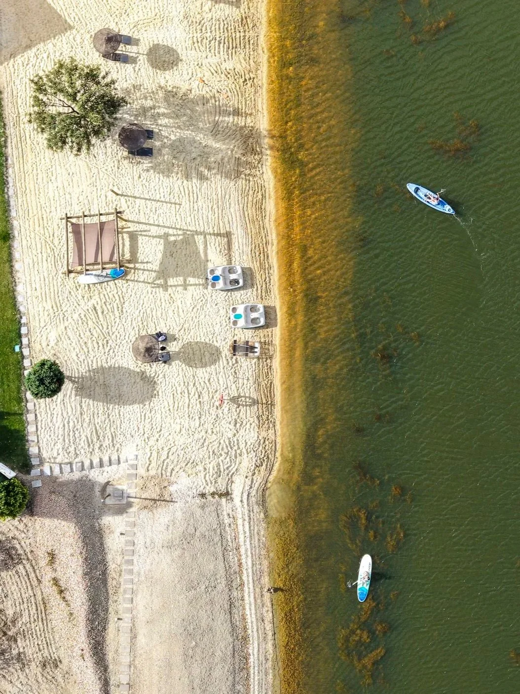 Drone view of the sandy lakeside beach with paddleboards, kayaks, and relaxing waterfront experiences