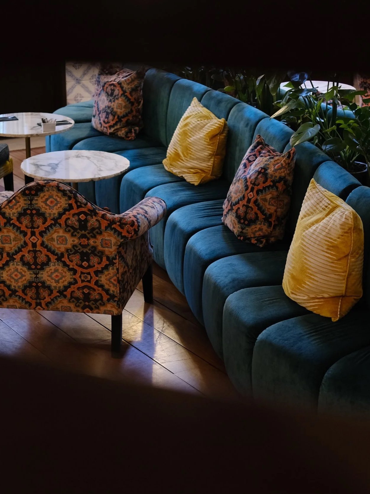 Stylish lounge with velvet seating, marble tables, and lush indoor greenery
