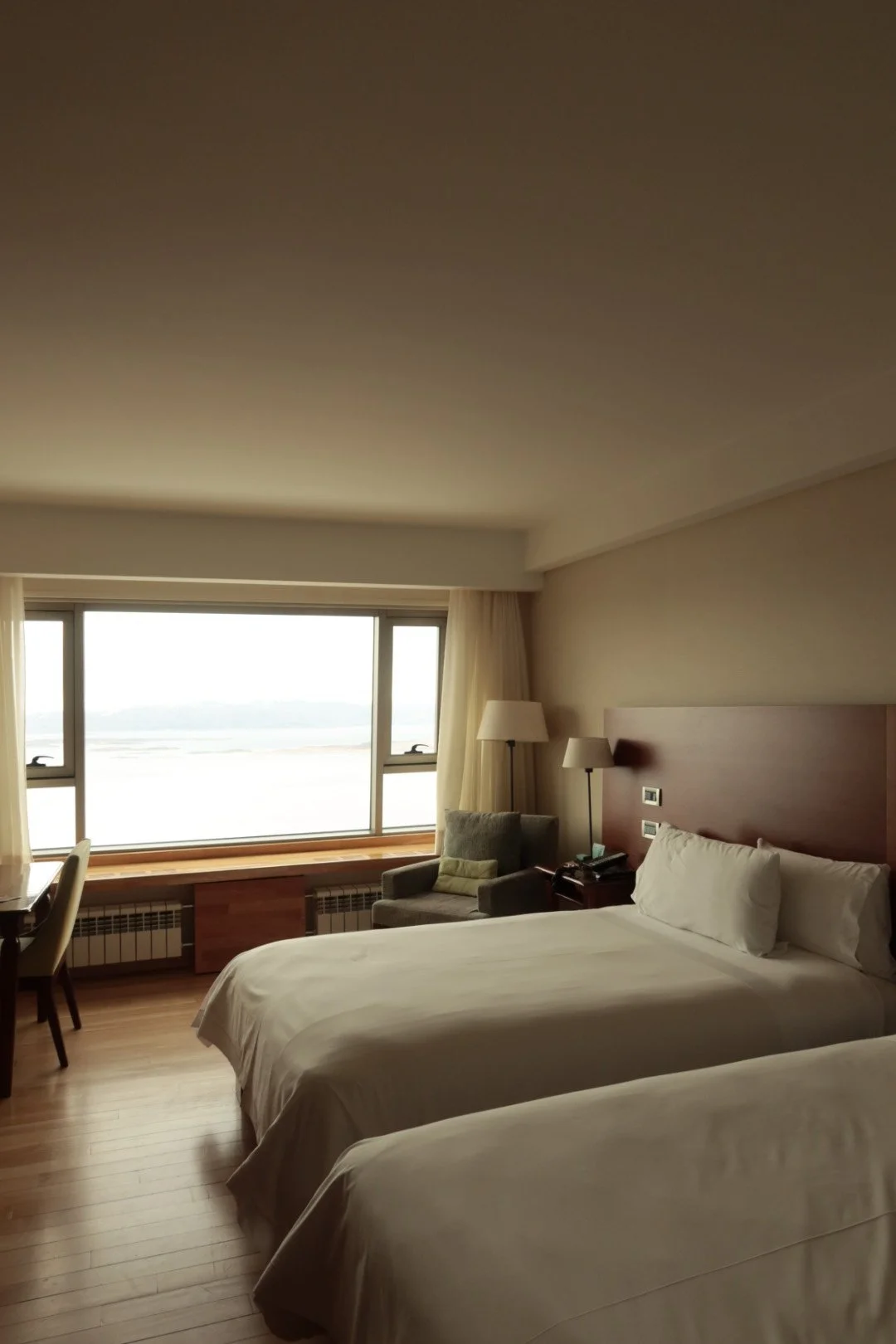 Bright guest room with two beds, warm wood flooring, and panoramic views across the Patagonian landscape