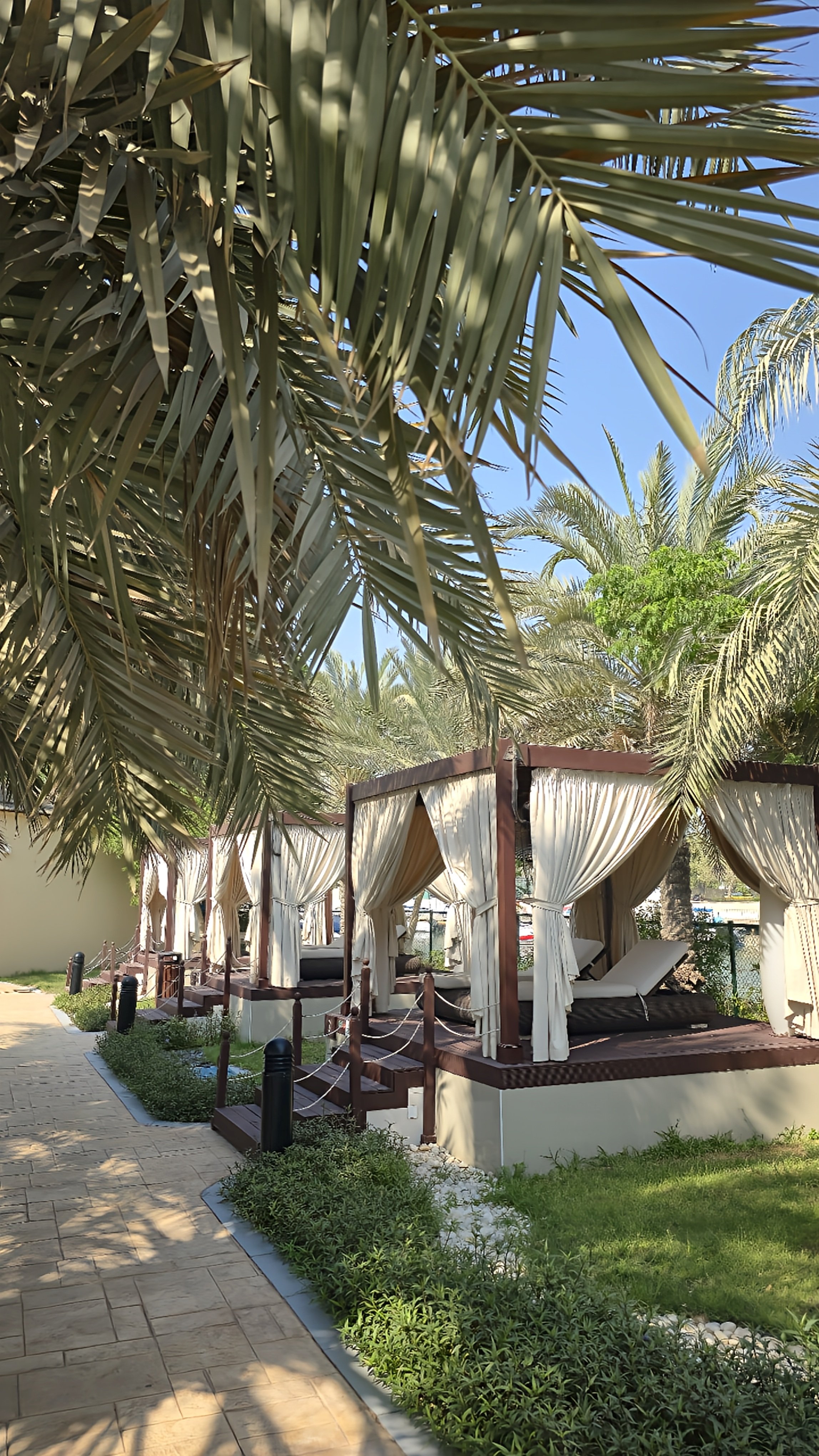 Private poolside cabanas with white curtains, comfortable loungers, wooden decks, and lush tropical landscaping