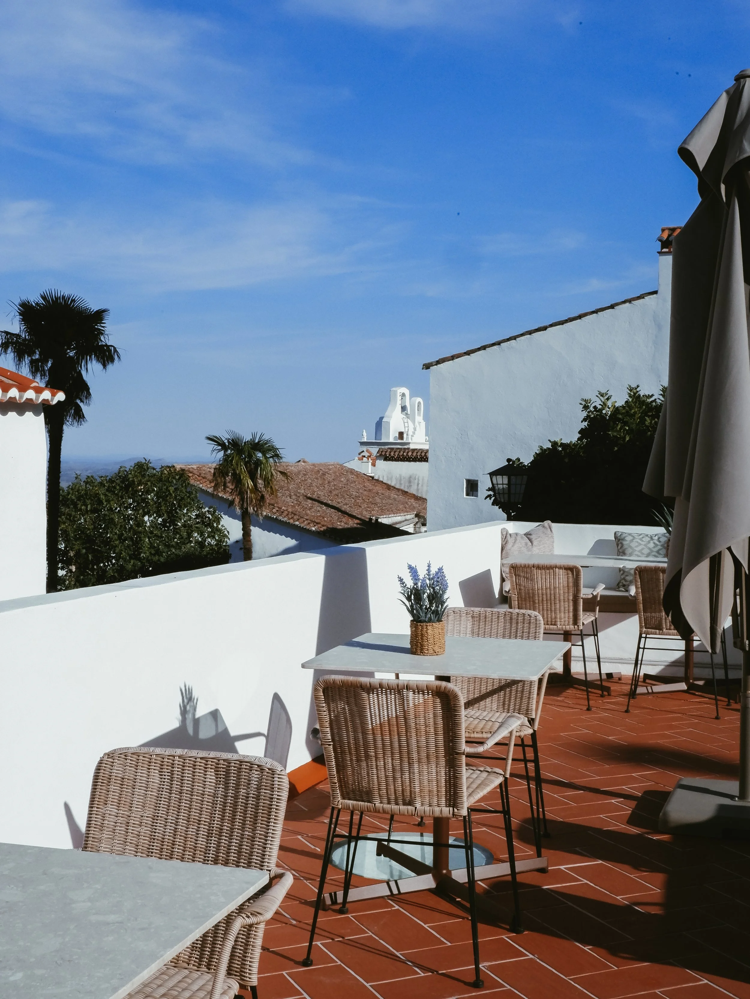 Sunny rooftop terrace with wicker seating overlooking Marvão's whitewashed houses and mountain landscape