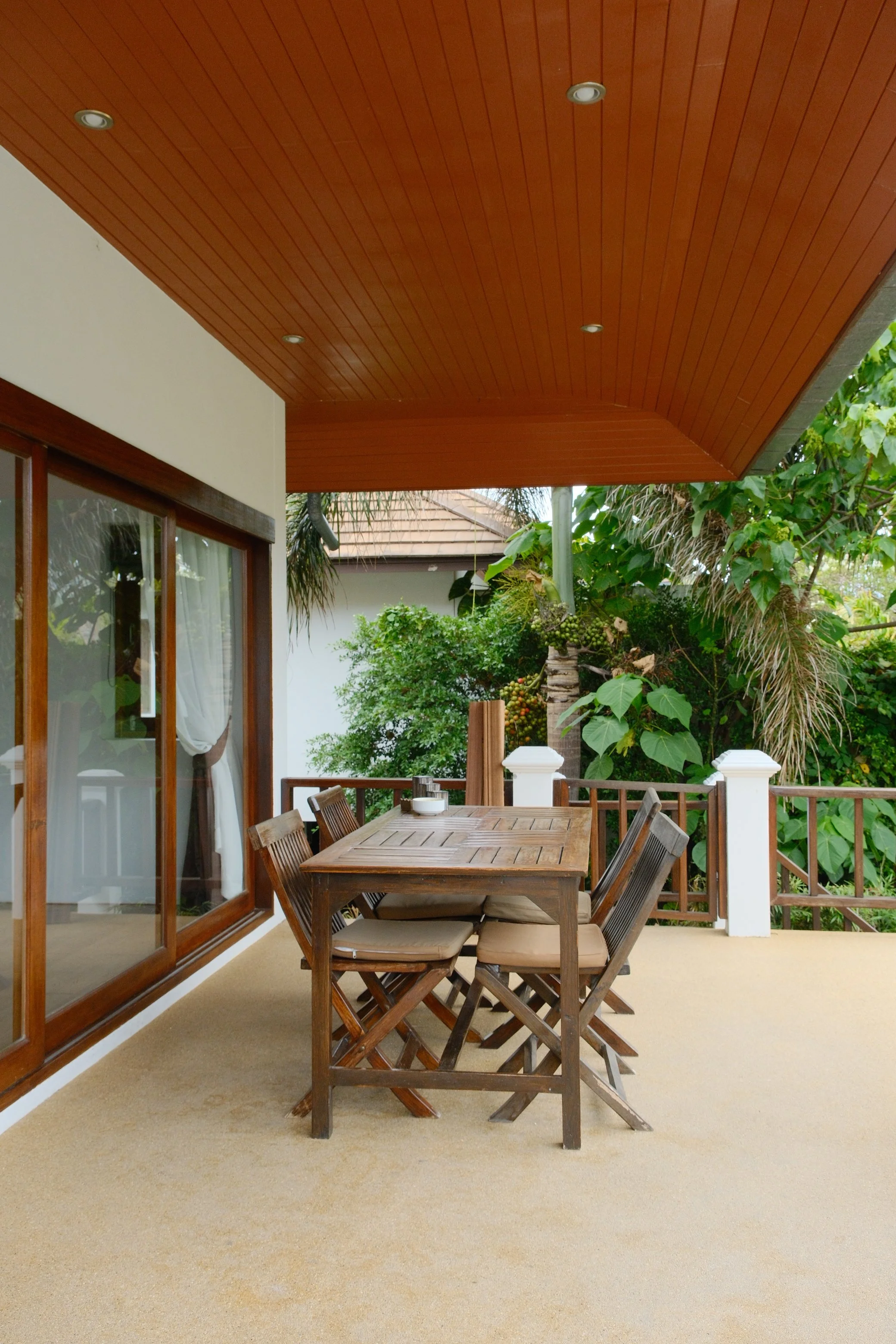 Covered private terrace with wooden dining furniture surrounded by lush tropical vegetation