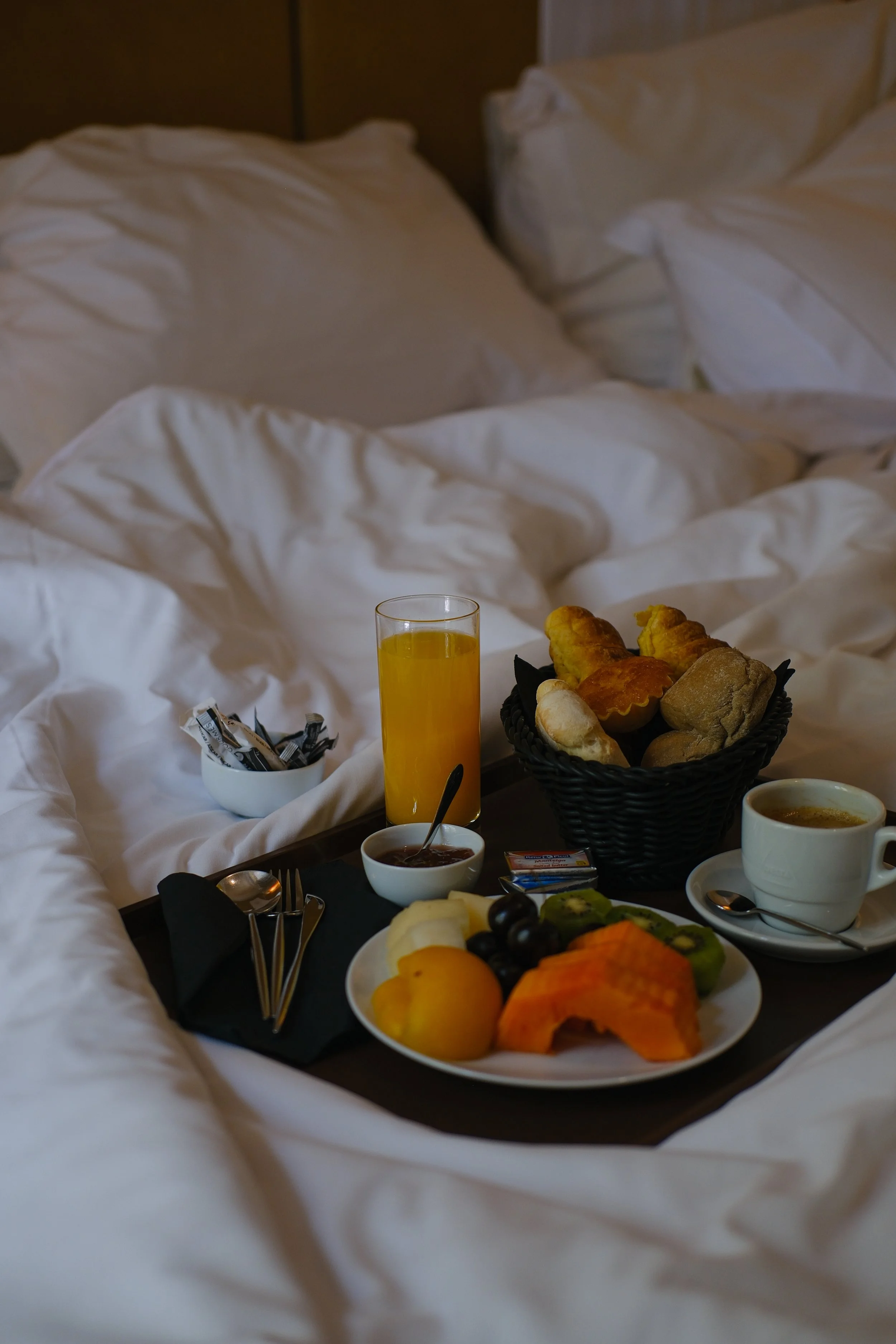 Breakfast in bed featuring fresh pastries, fruit, coffee, and orange juice