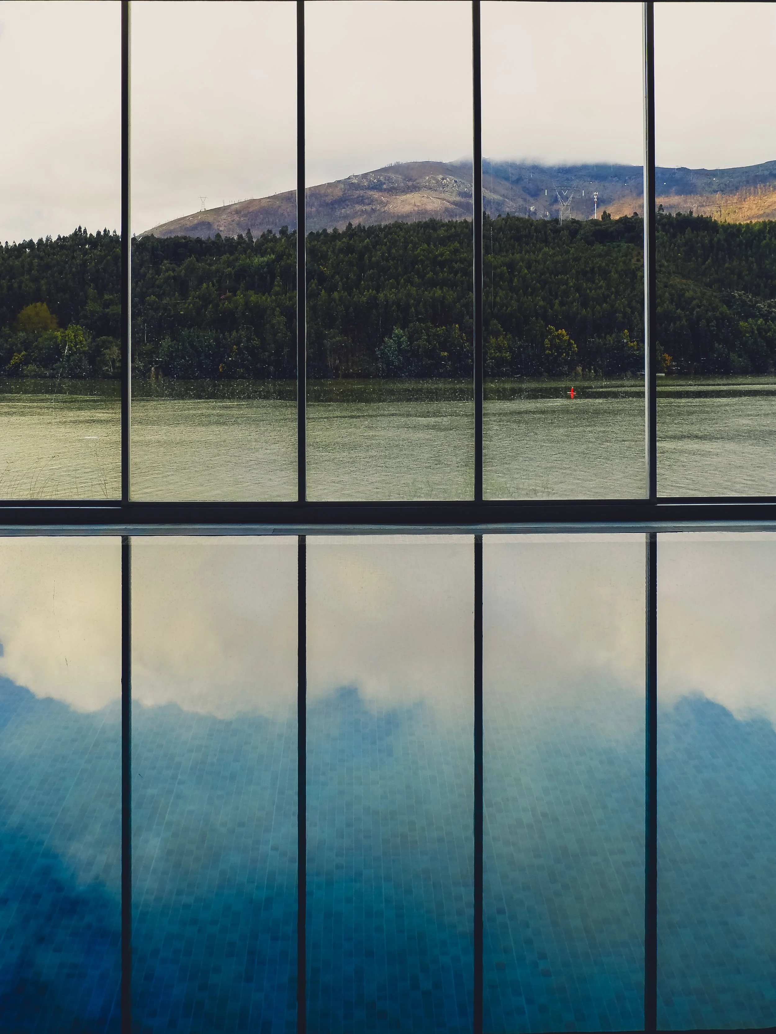Indoor infinity pool reflecting mountain and river scenery through expansive glass walls, Octant Douro – Castelo de Paiva, Portugal.