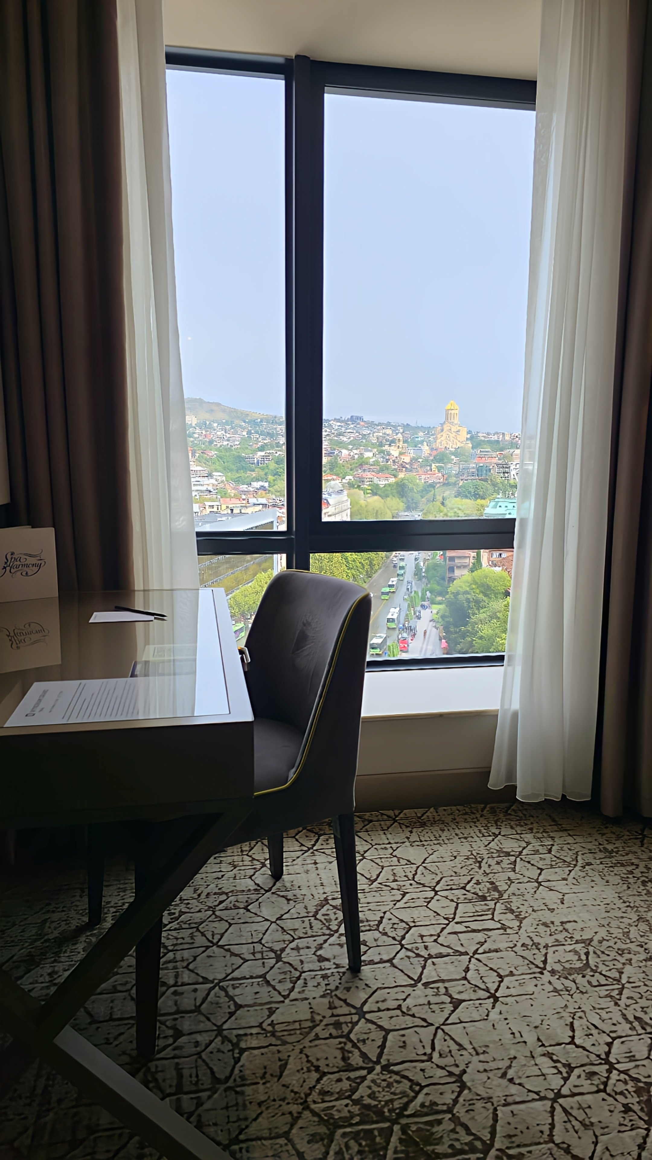 Guest room workspace beside panoramic windows overlooking the Tbilisi cityscape