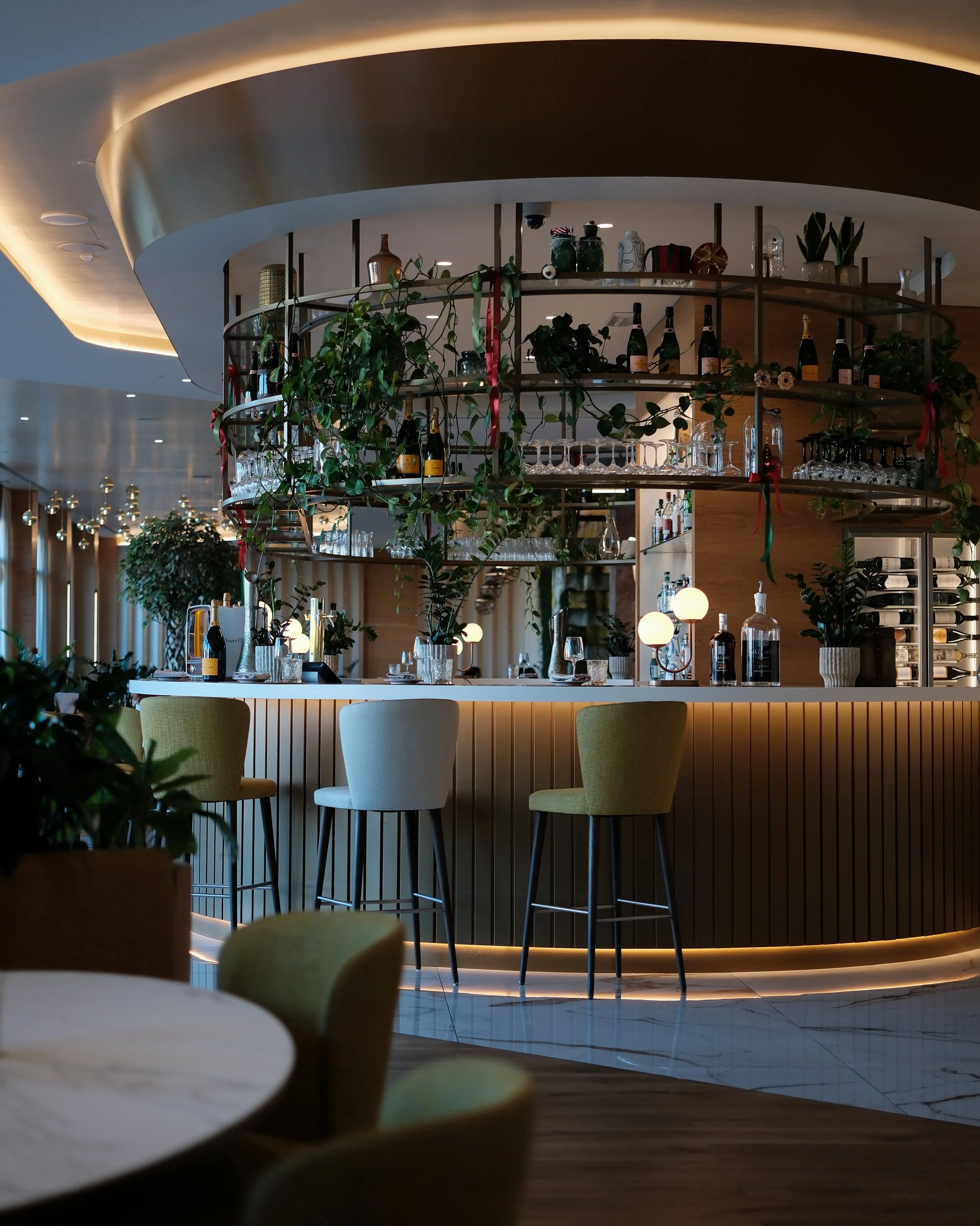 Stylish bar with curved shelving, hanging greenery, soft ambient lighting, and colorful seating — Hyatt Regency Lisbon