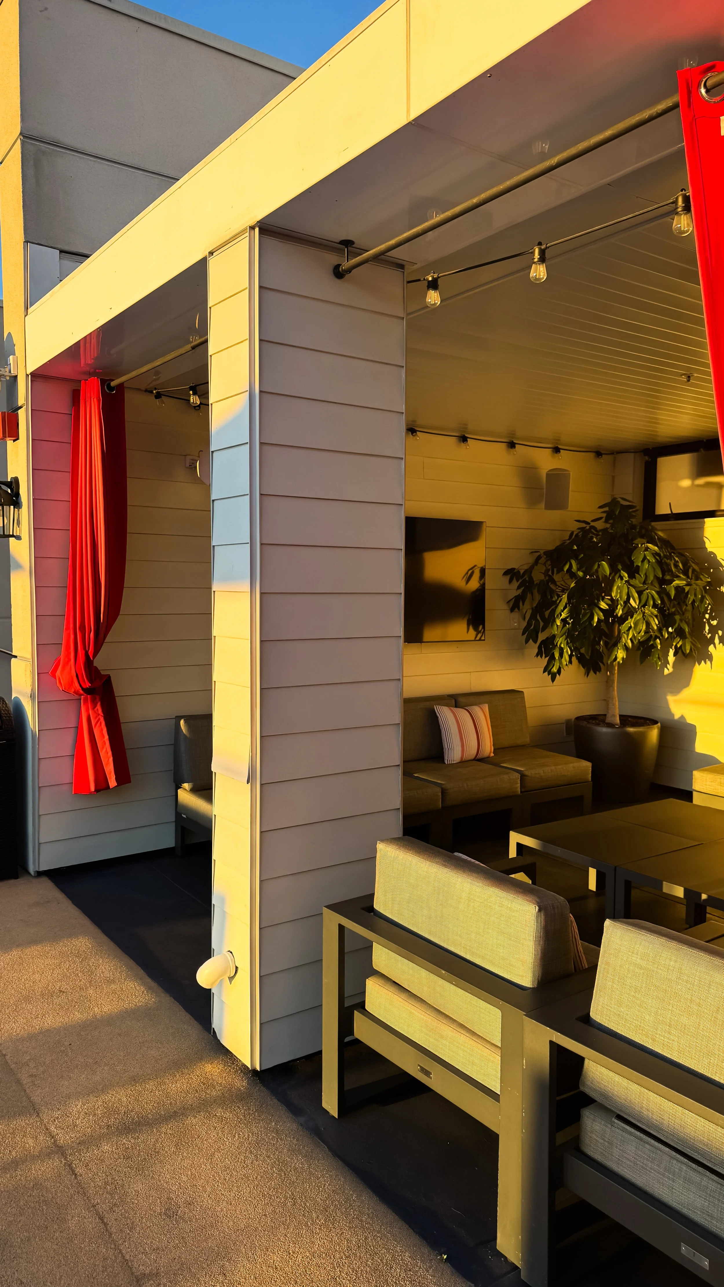 Private cabana lounge with red curtains, warm sunset light, and modern outdoor seating on the rooftop terrace, Andaz San Diego – San Diego, California.