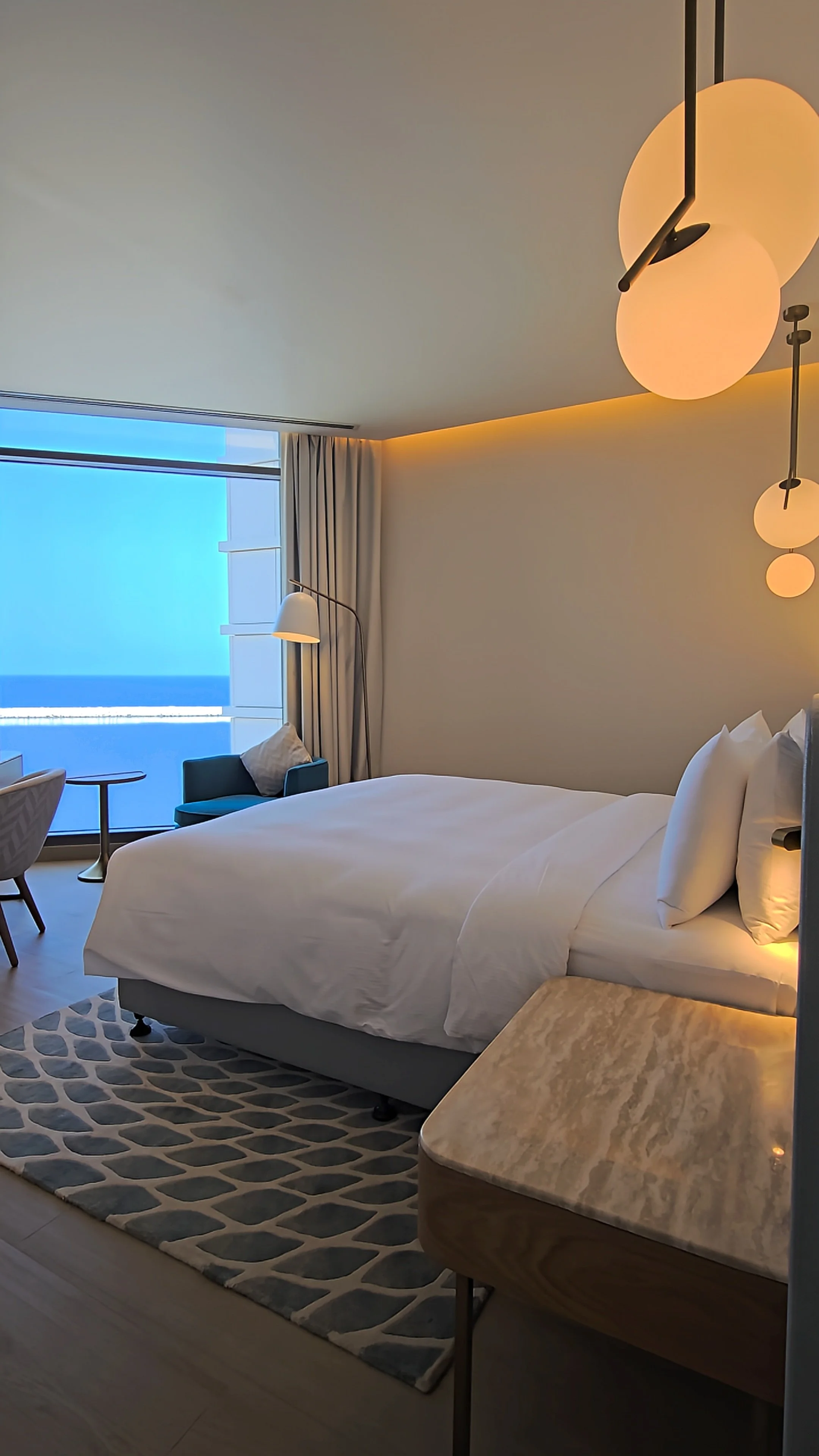 Contemporary guest room featuring a king-size bed, elegant pendant lighting, comfortable seating, and Arabian Sea views
