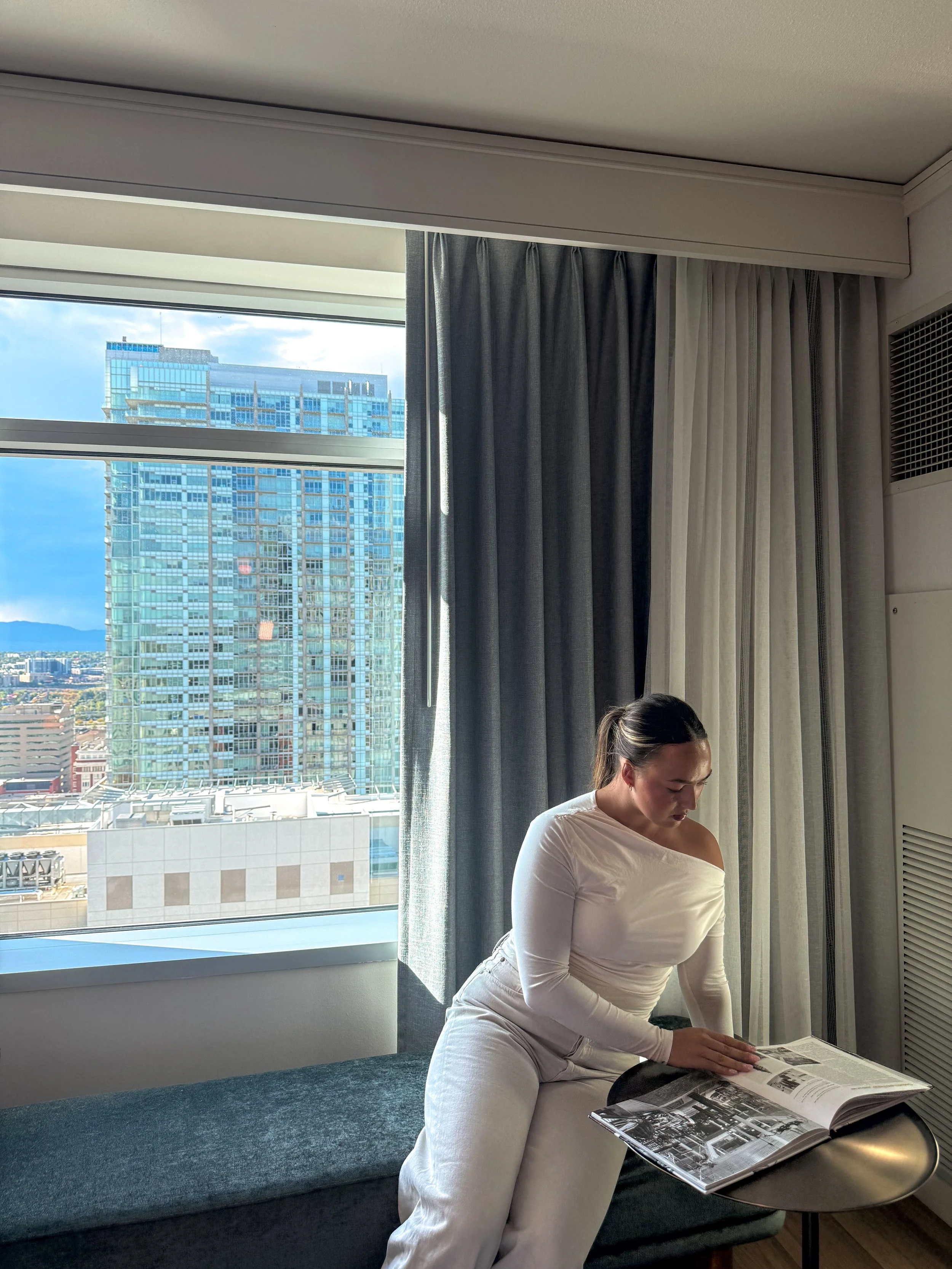 Guest relaxing beside a large hotel room window with panoramic views of downtown Denver