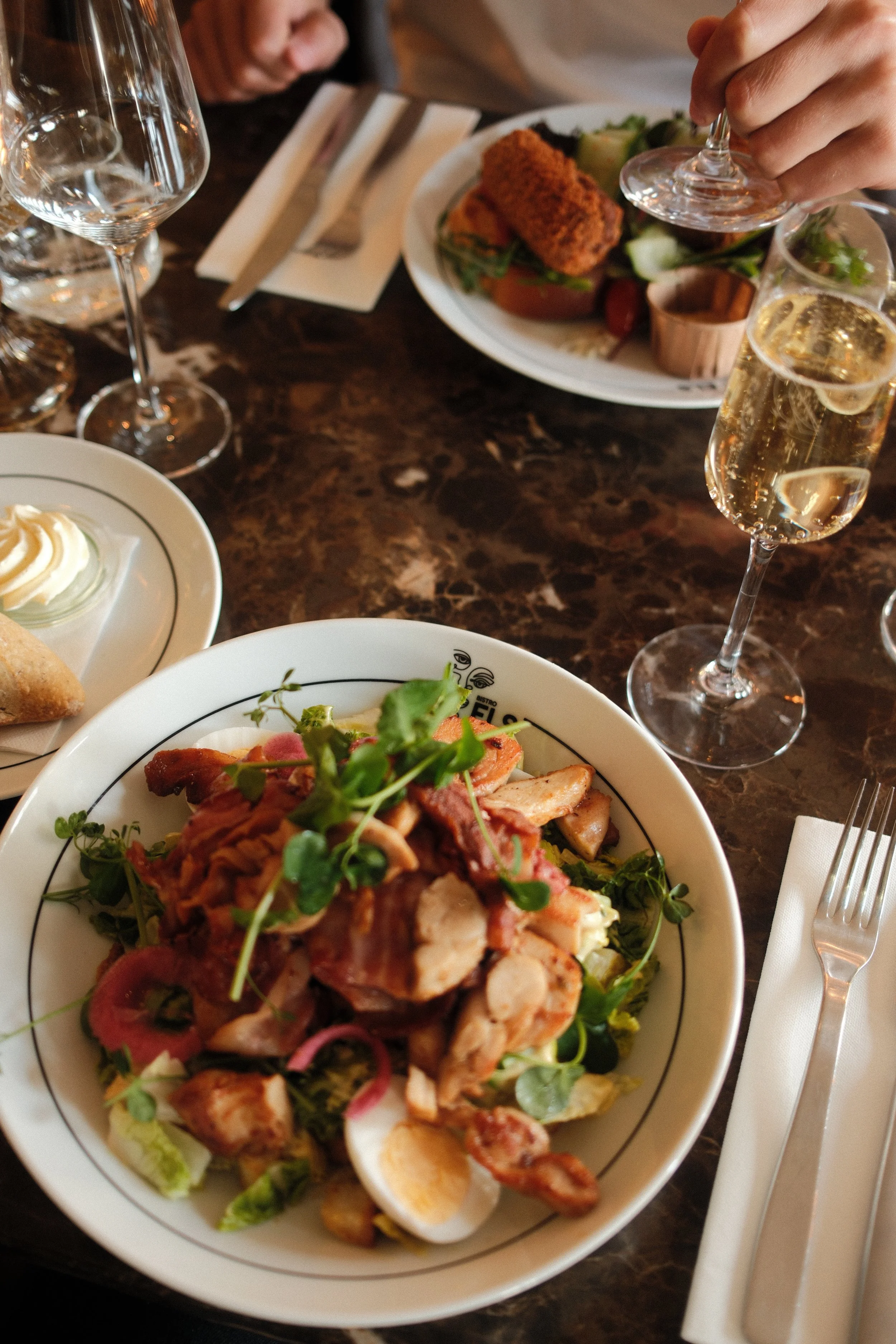 Fresh salad with crispy bacon, soft egg, and microgreens paired with sparkling wine on a marble table, Château St. Gerlach – Vaeshartelt Maastricht.