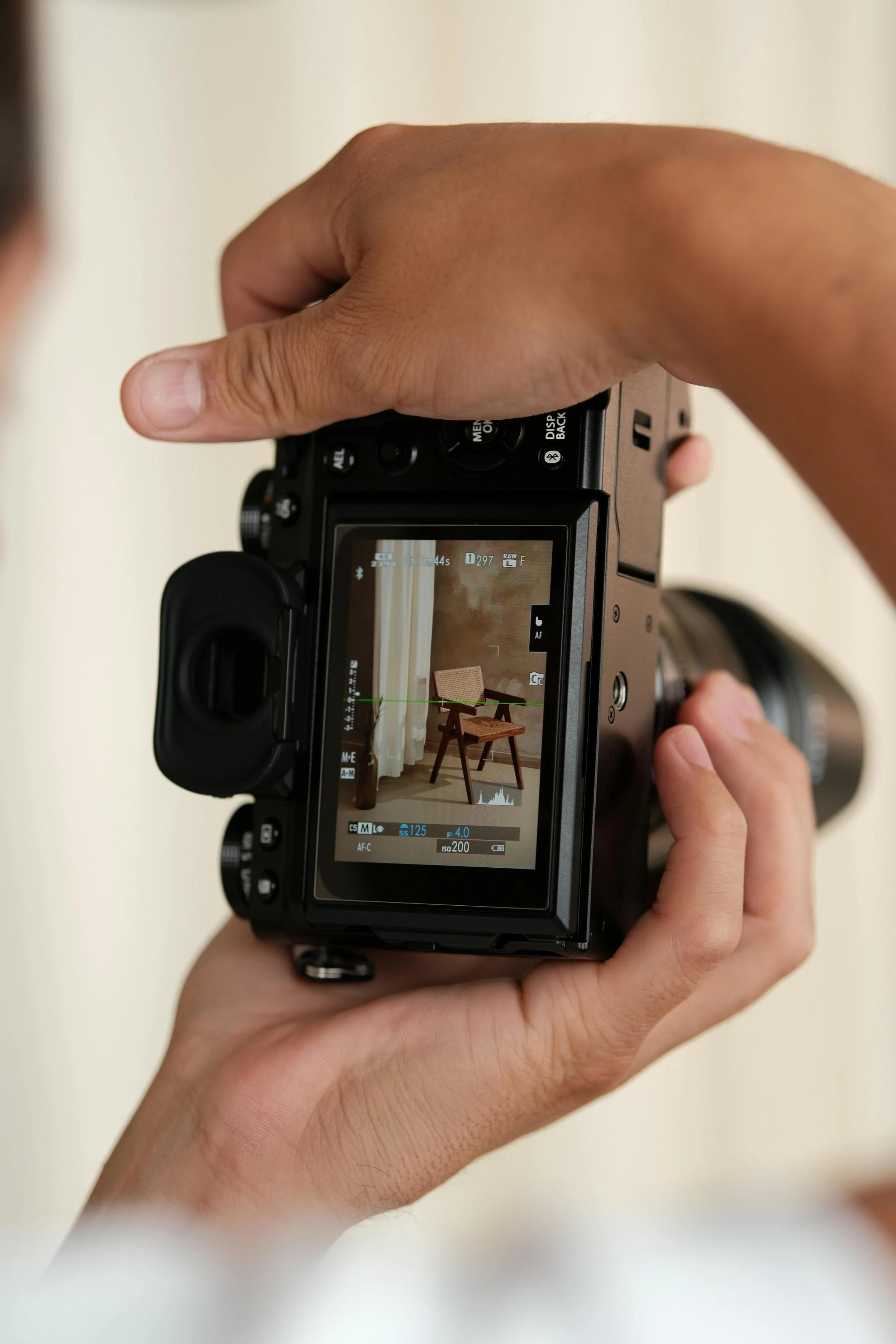Close-up of a person holding a digital camera, focusing on a shot of a wooden chair in front of a curtain - content creator composing a picture.