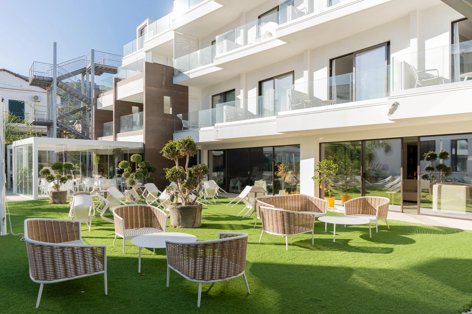 Outdoor garden lounge with white chairs and green turf at Sunset Hotel Cefalù