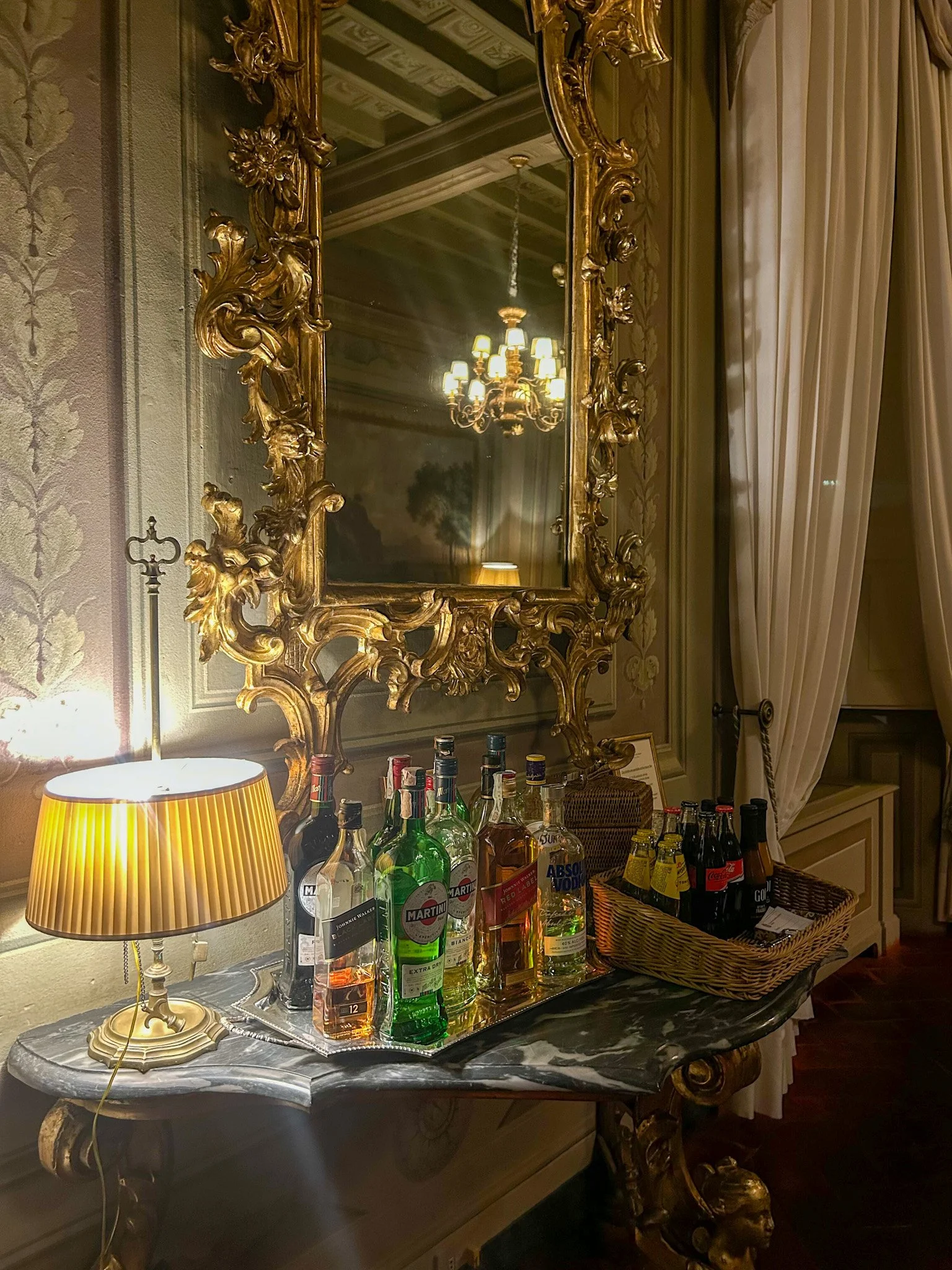 Historic palace lounge with ornate gilded mirror, marble console, and elegant selection of premium spirits in Palazzo Niccolini al Duomo