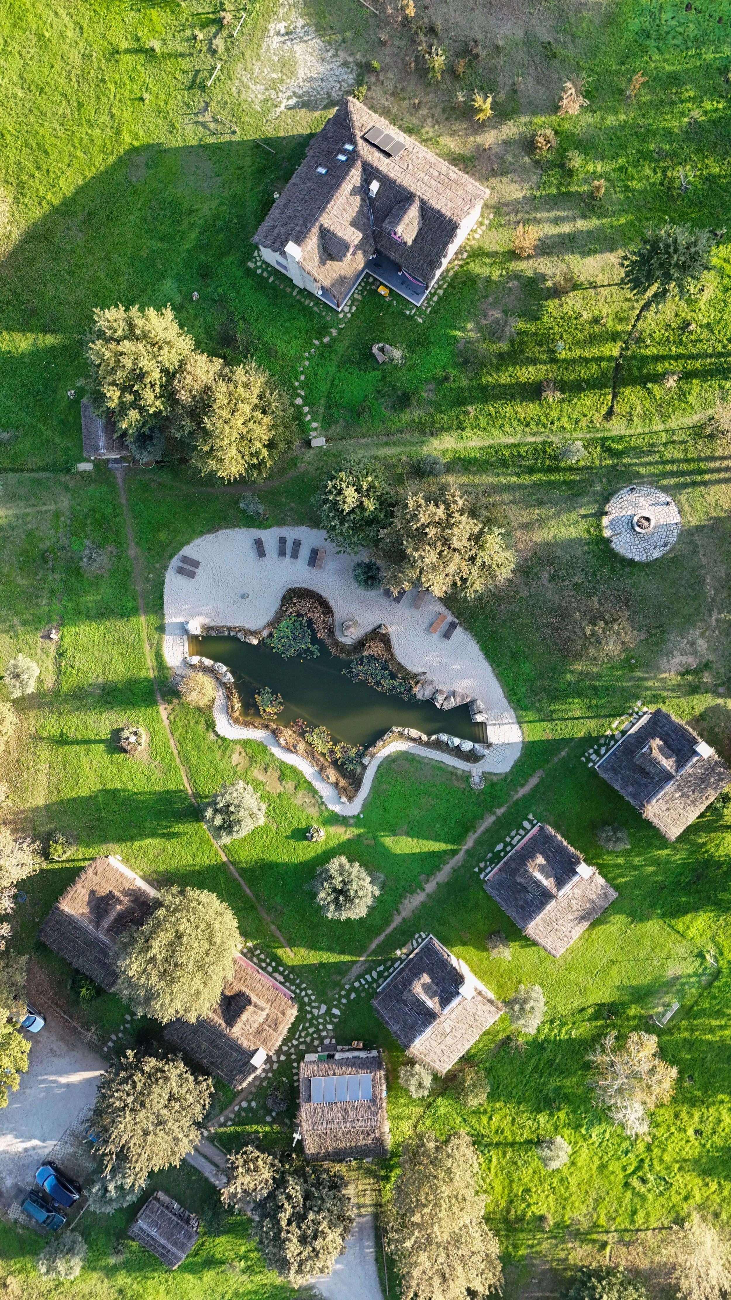 Aerial view of Chão do Rio with traditional stone cottages, natural swimming pond, and green countryside in Serra da Estrela