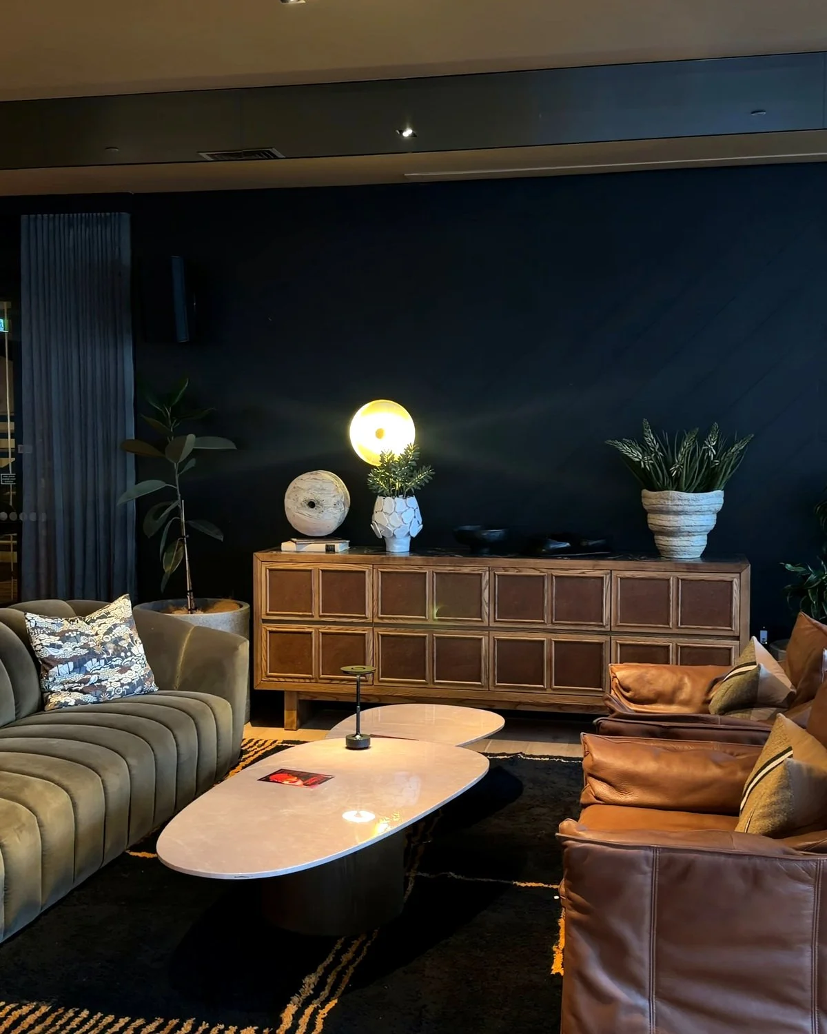 Elegant lounge area with leather sofas, a curved green velvet couch, marble coffee tables, and warm ambient lighting