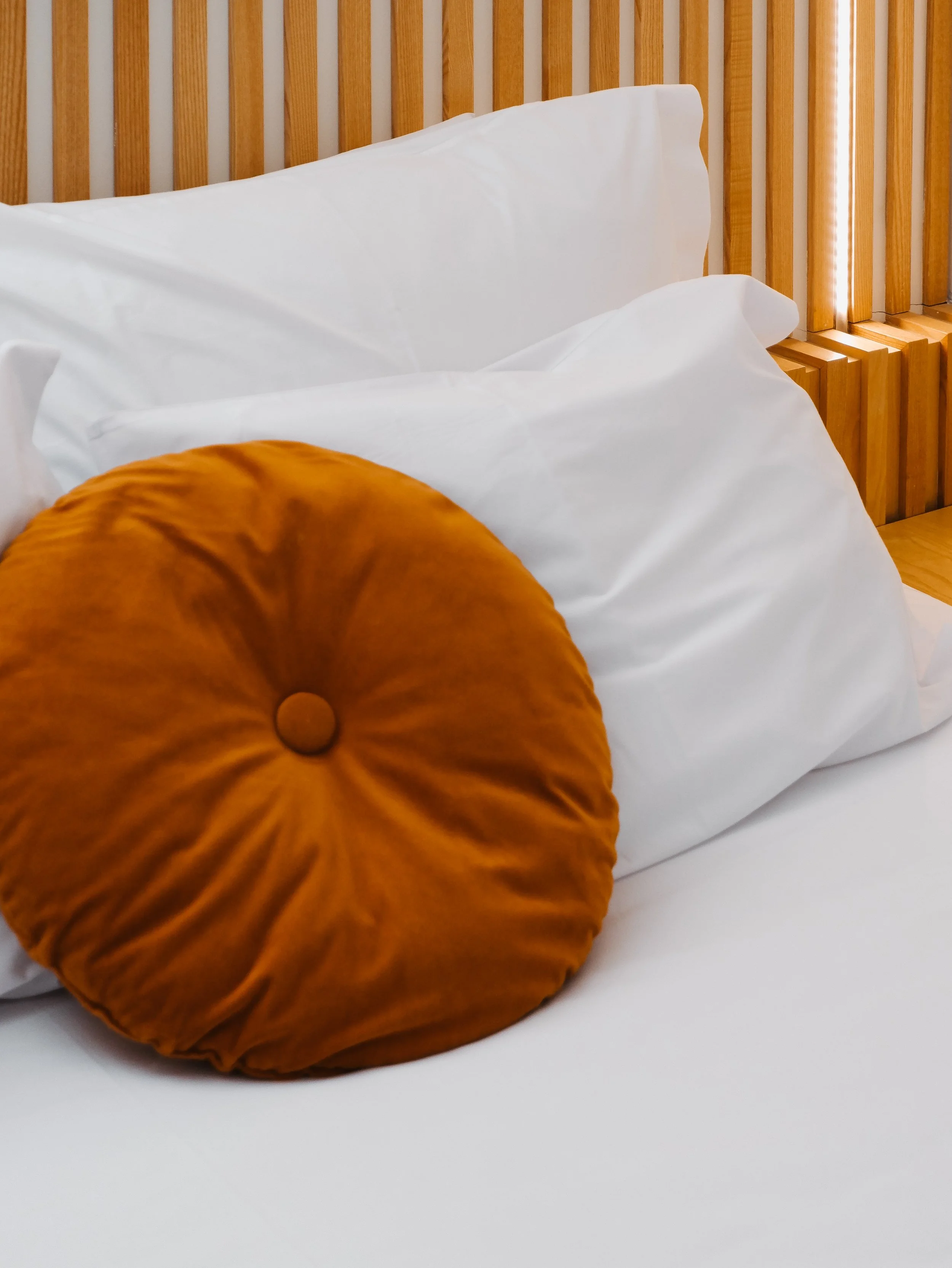 Soft linen bedding with handcrafted velvet cushion and warm natural wood details
