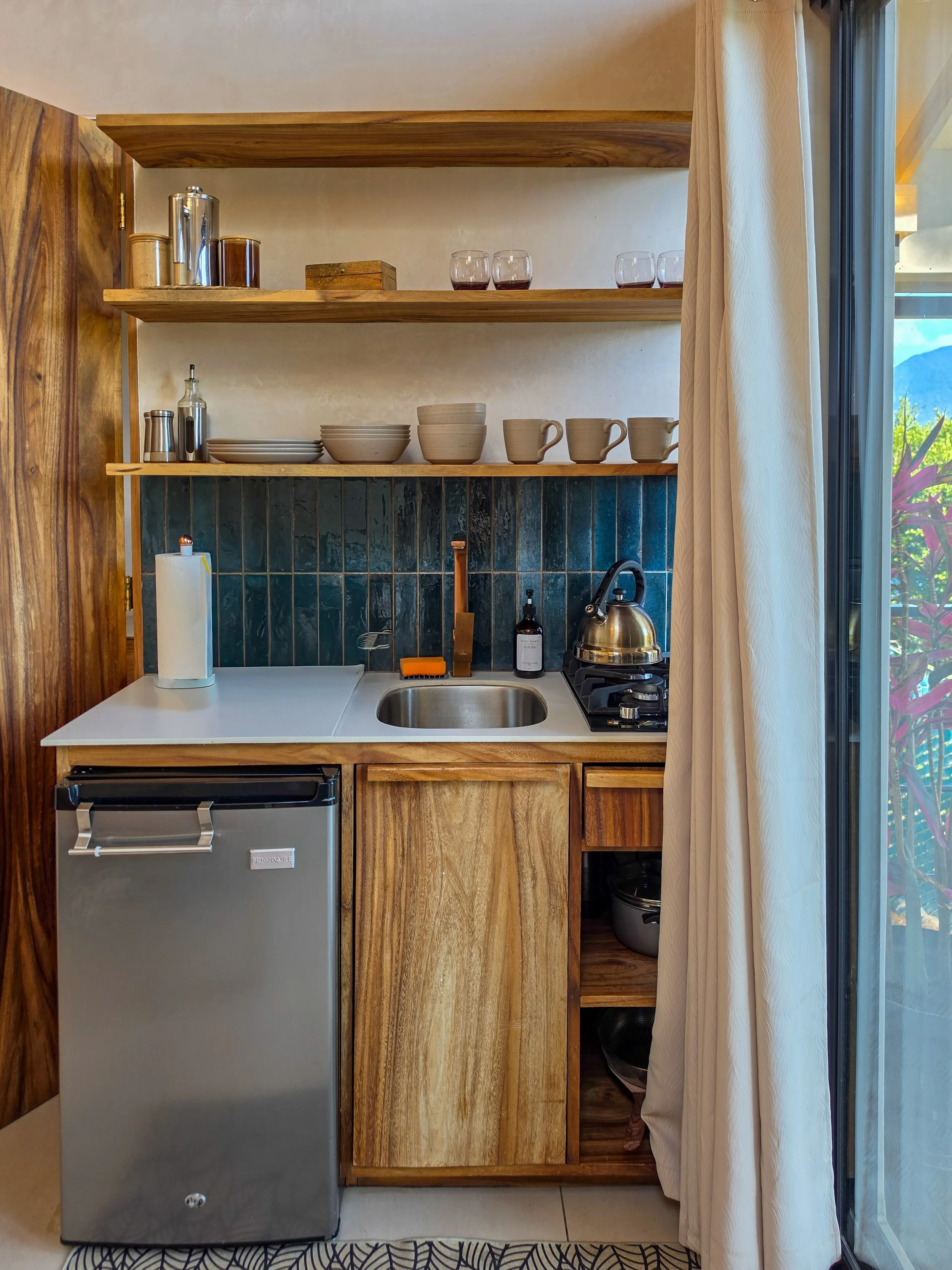 Compact kitchenette with handcrafted wooden cabinetry and ceramic tableware
