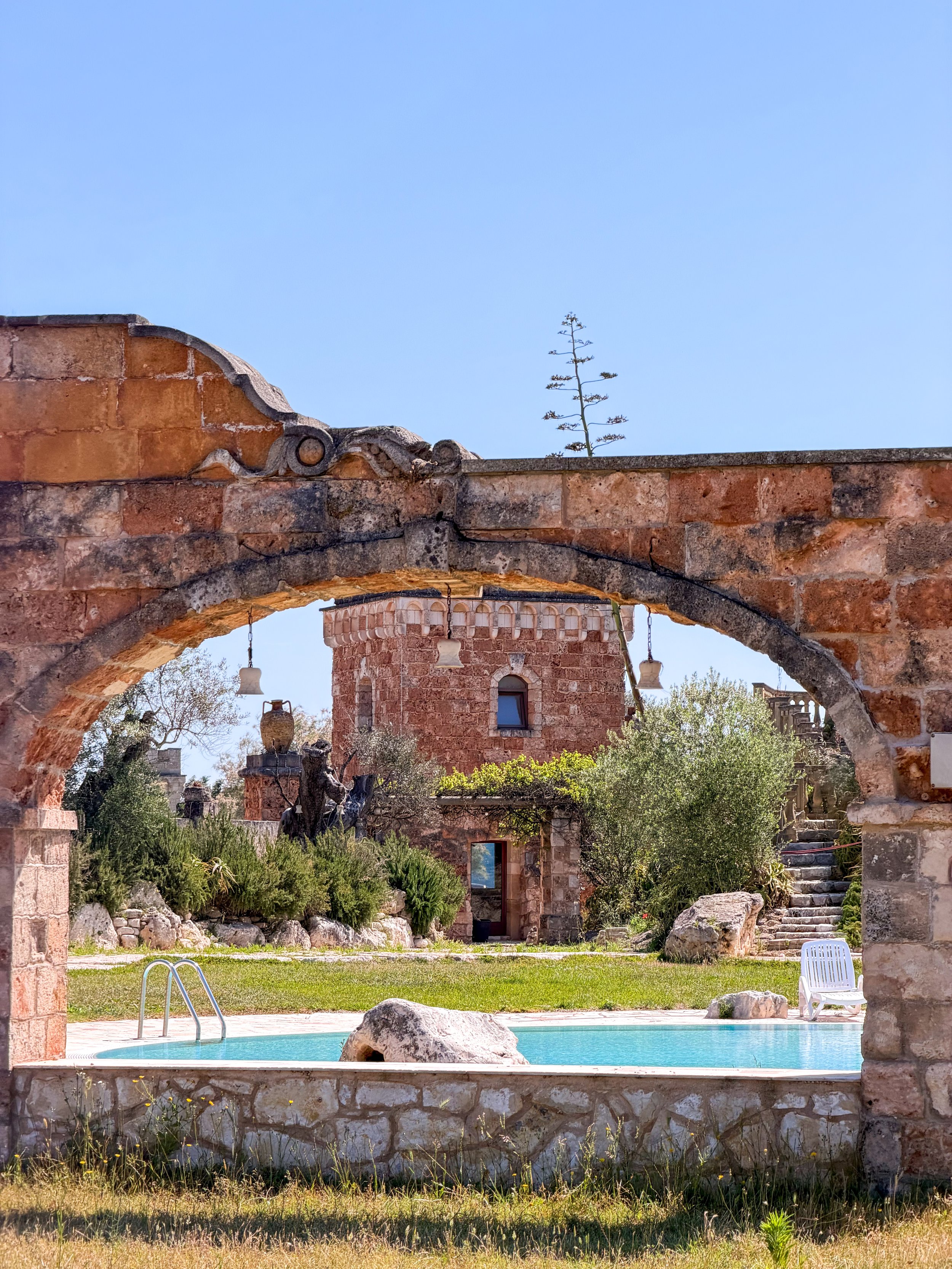 Historic stone arches framing the swimming pool and iconic estate buildings at Tenute Al Bano, Puglia