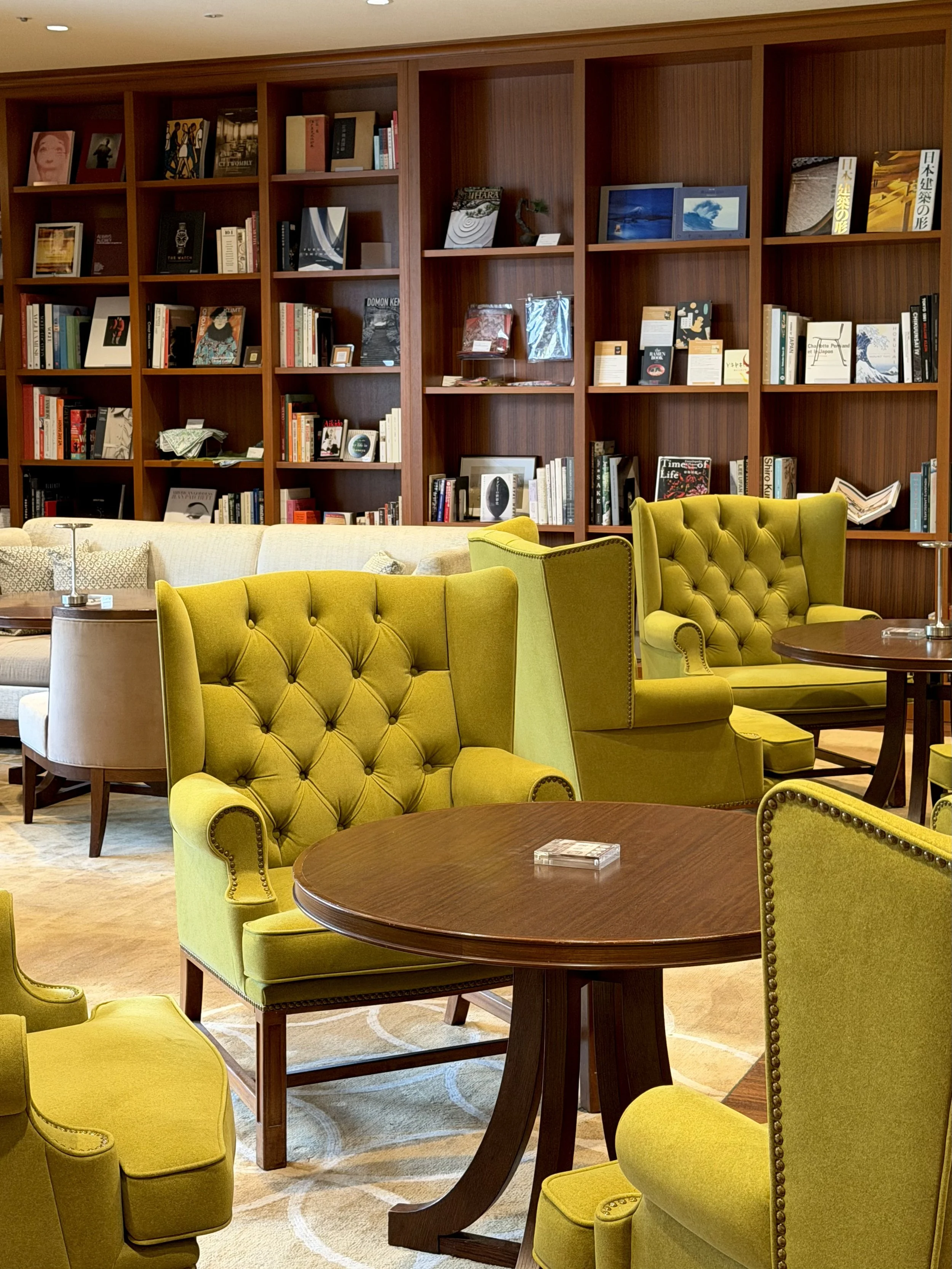 Library lounge with green tufted armchairs, wooden tables, and floor-to-ceiling bookshelves