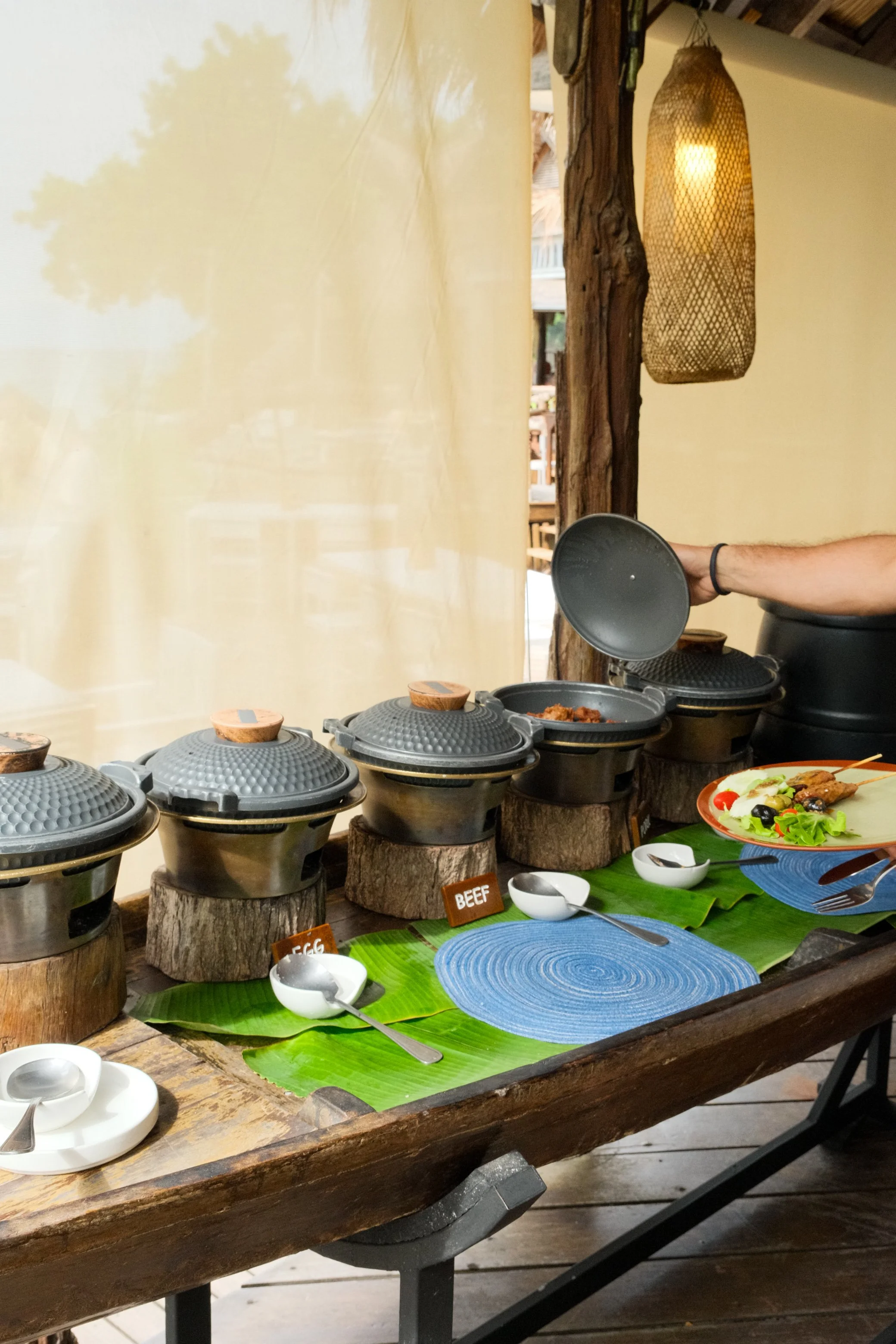 Breakfast station with hot dishes served in rustic cookware over banana leaves and natural wood
