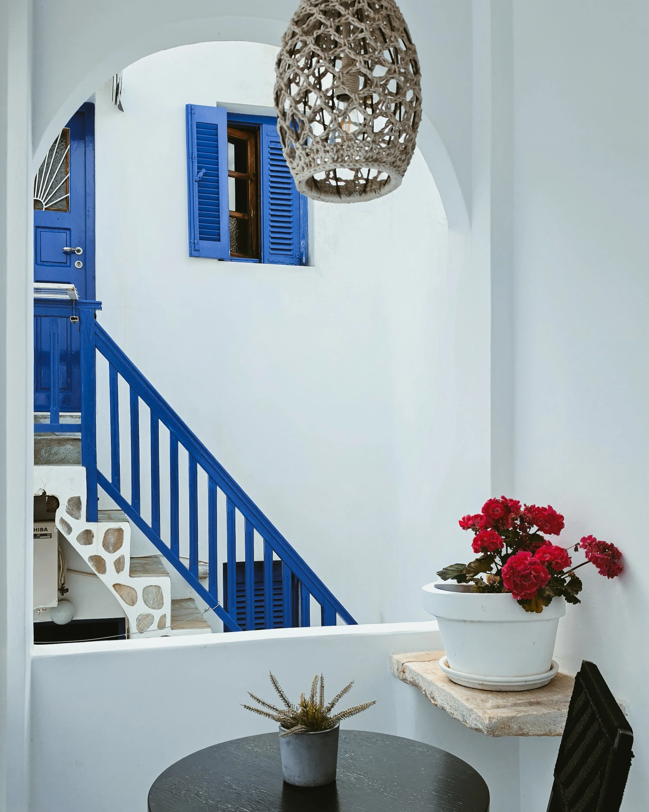 Traditional Cycladic courtyard with whitewashed walls, blue shutters, and vibrant Mediterranean flowers