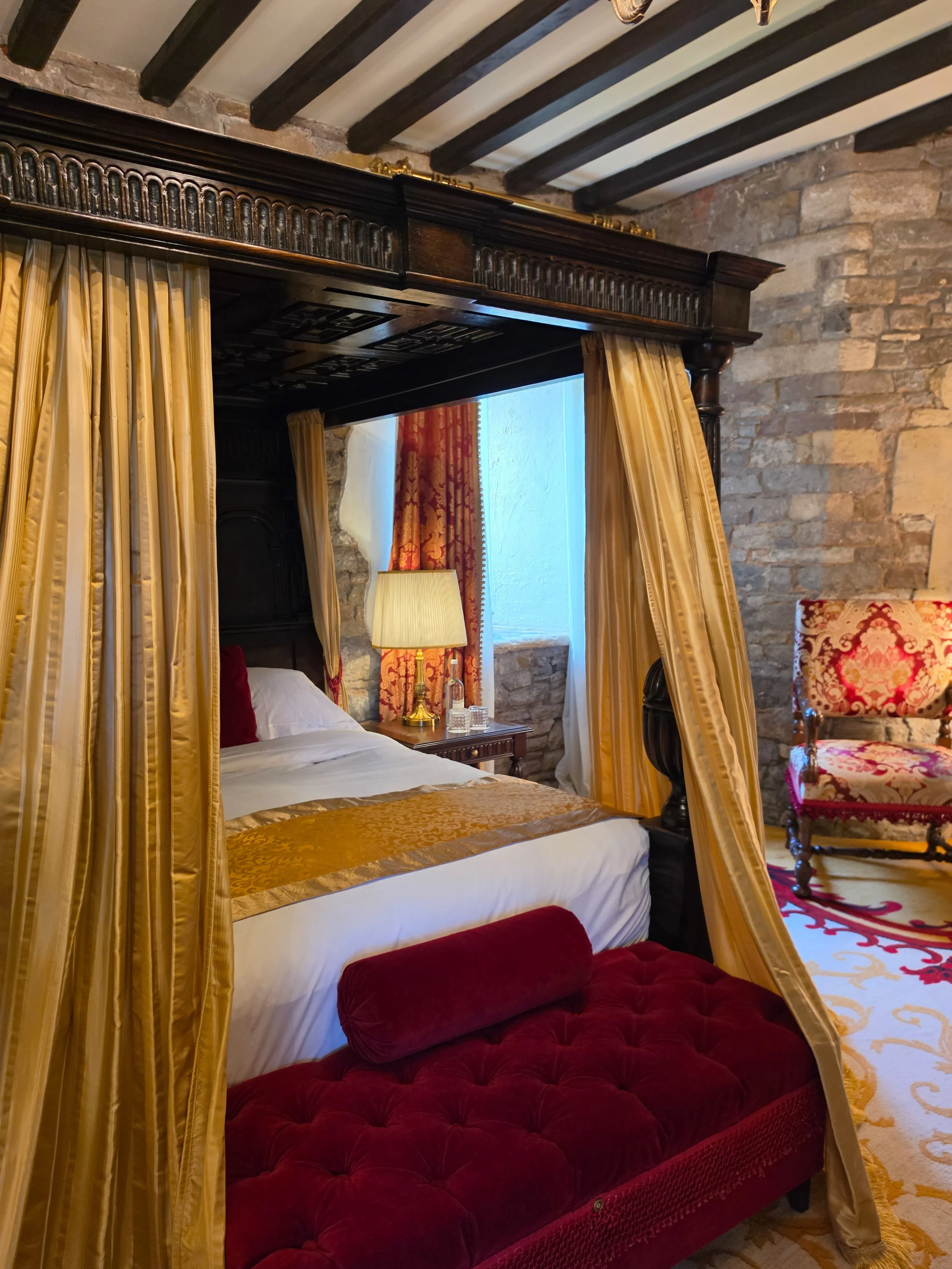 Luxurious four-poster bedroom with rich fabrics, exposed stone walls, and royal-inspired décor