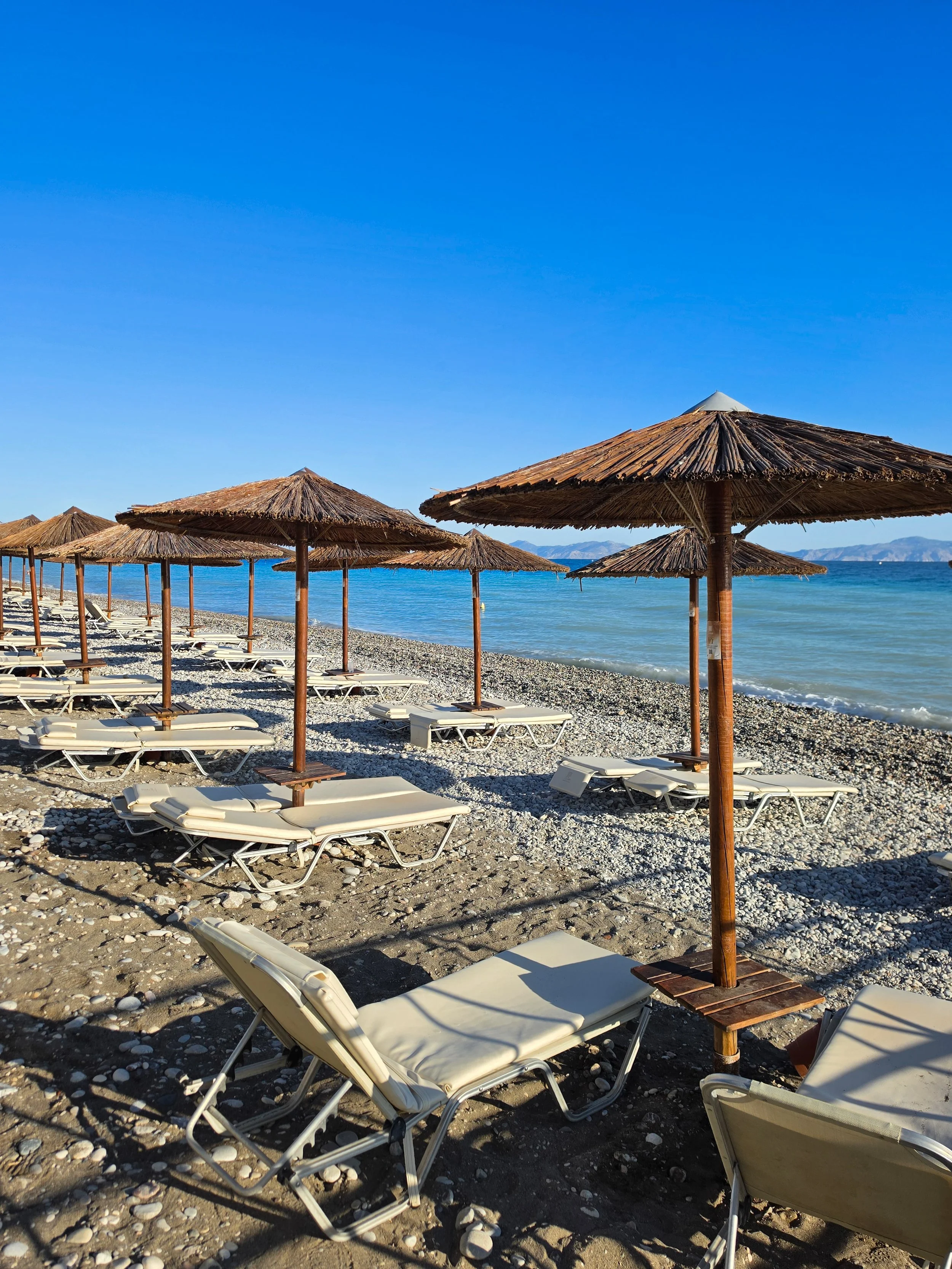 Private pebble beach lined with sun loungers overlooking crystal clear waters