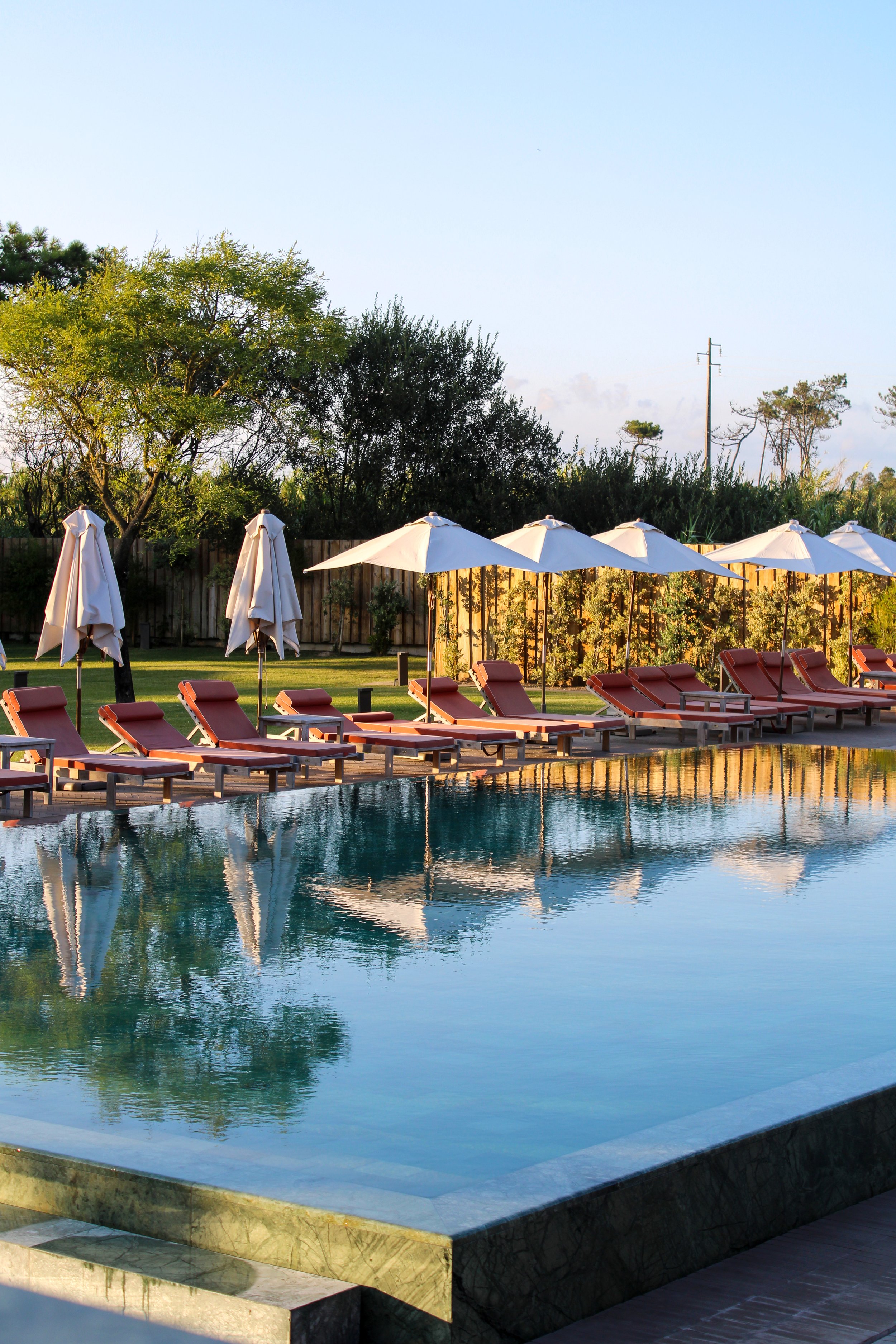 Outdoor swimming pool lined with sun loungers and relaxing garden spaces