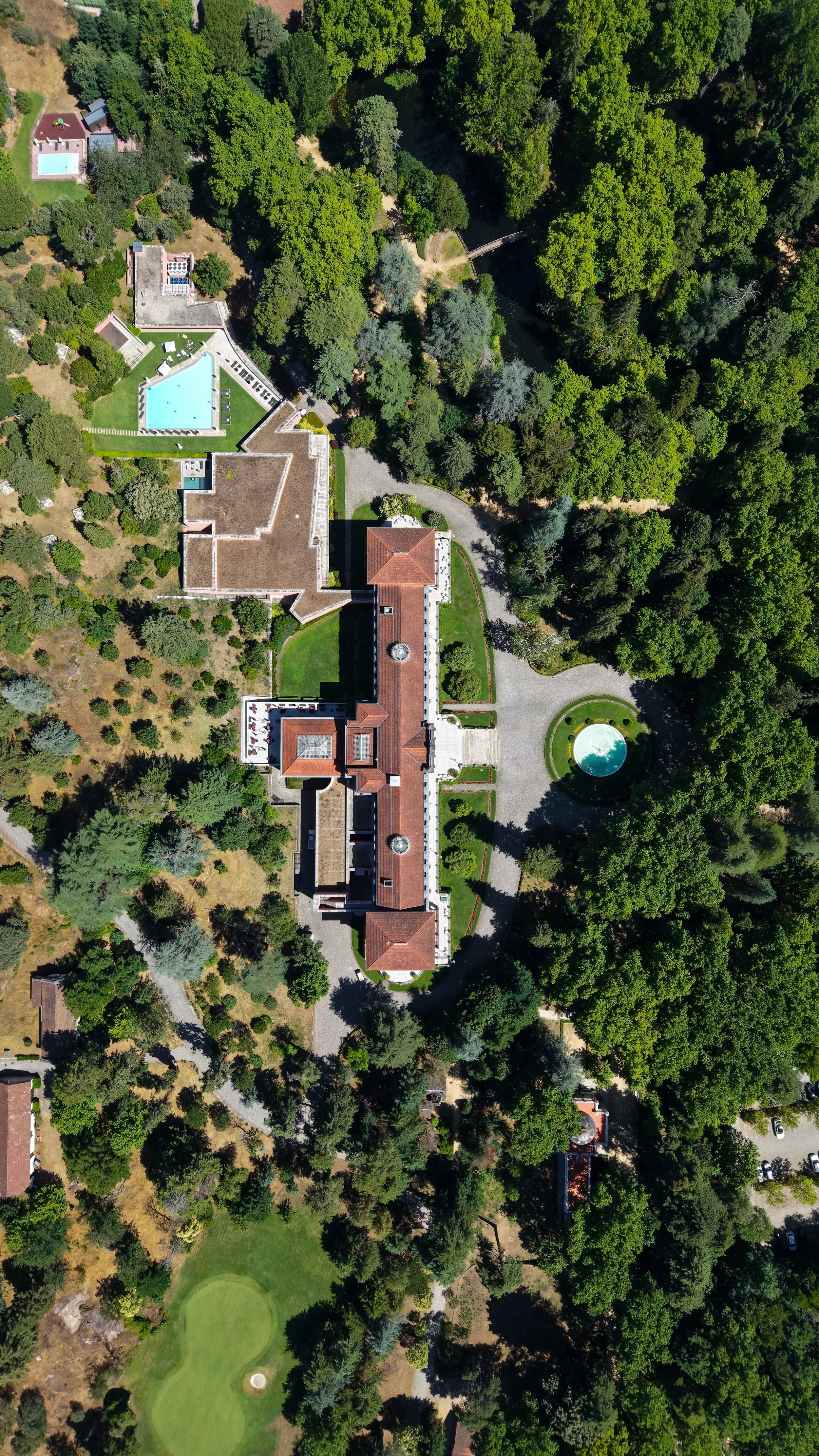 Aerial view of a historic luxury resort surrounded by lush forests, landscaped gardens, golf course, and outdoor pools
