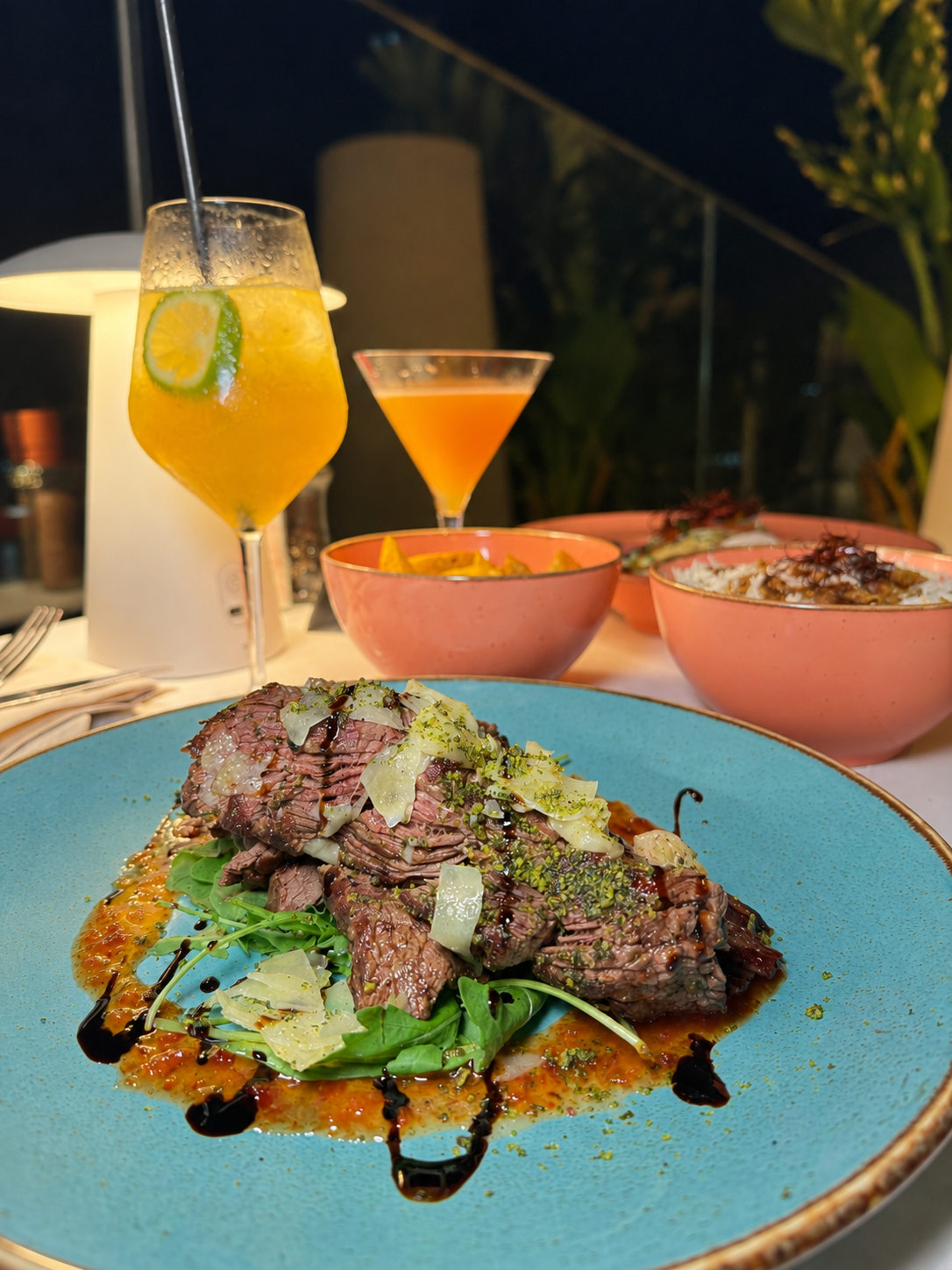 Grilled beef served with fresh greens, shaved cheese, rich sauce, and cocktails