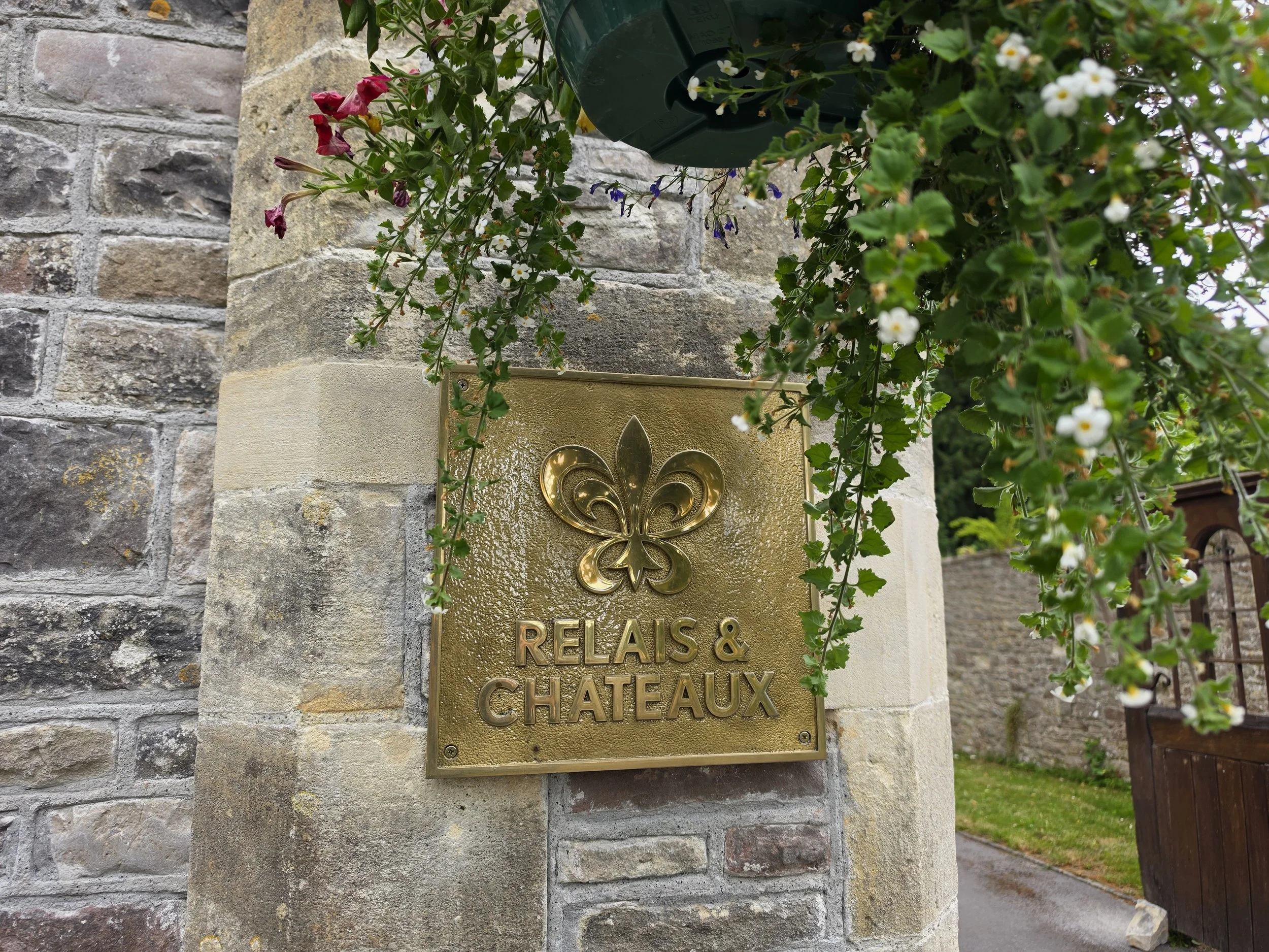 Image Metadata
Relais & Châteaux plaque displayed at the entrance of a historic luxury castle hotel surrounded by stone architecture and lush gardens