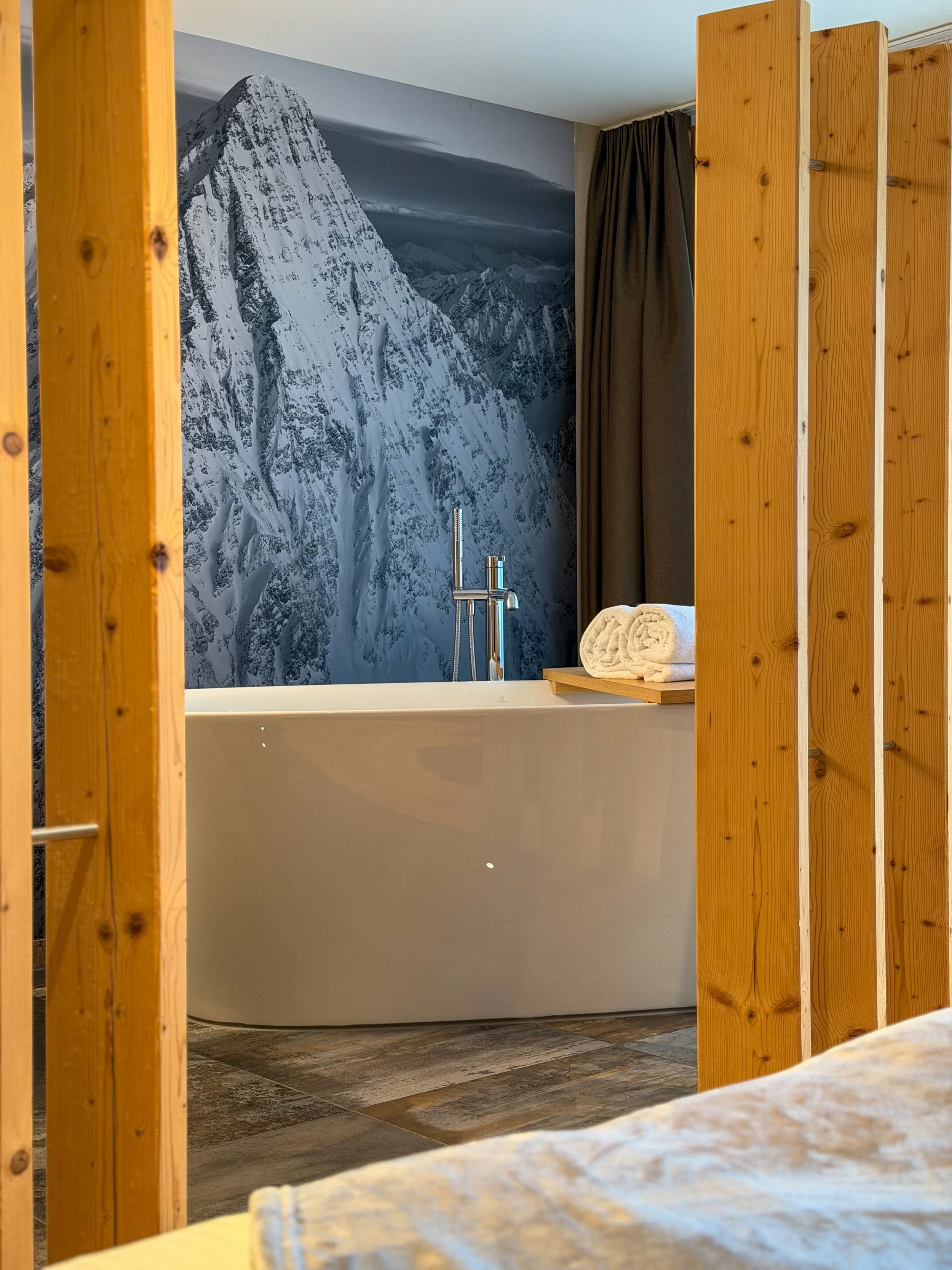 Freestanding bathtub framed by a dramatic alpine peak mural inside a suite at Eiger Mountain & Spa Soul Resort, Switzerland