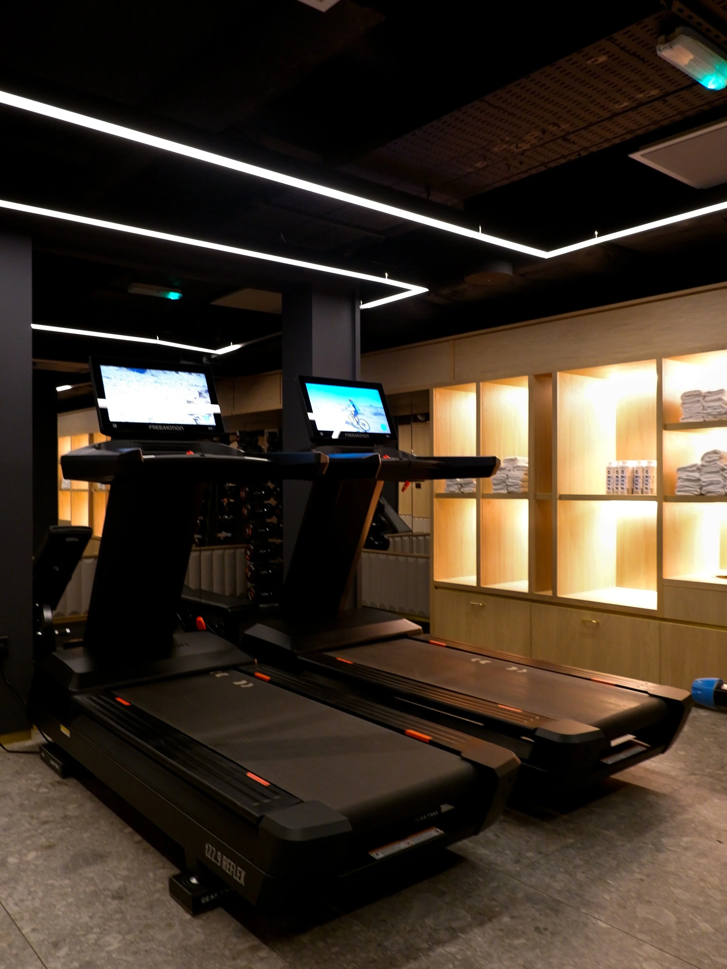 Modern hotel fitness centre featuring treadmills, illuminated storage shelves, and contemporary lighting