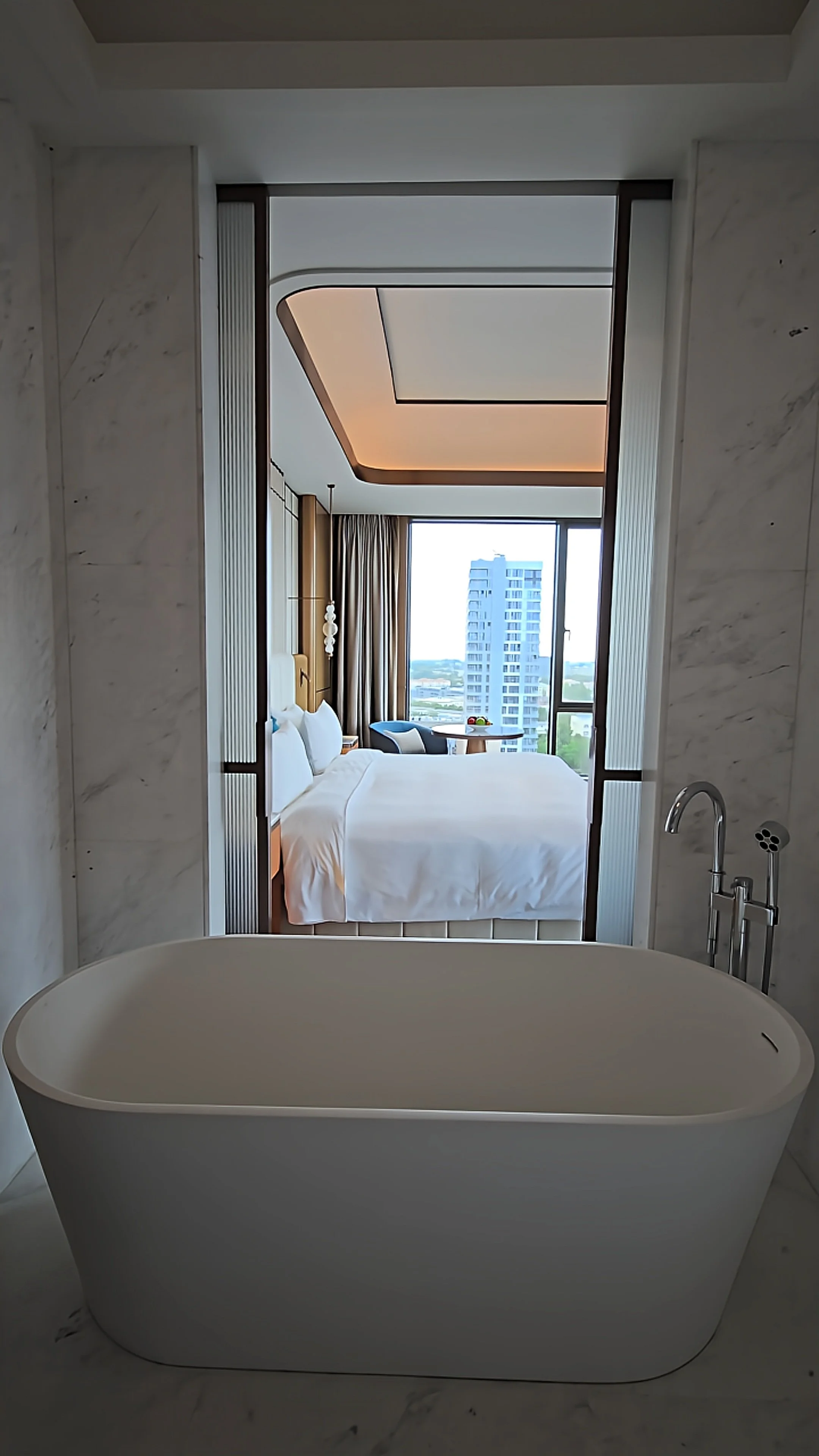 Contemporary marble bathroom with a freestanding bathtub opening into a spacious guest room at JW Marriott Hotel Tashkent