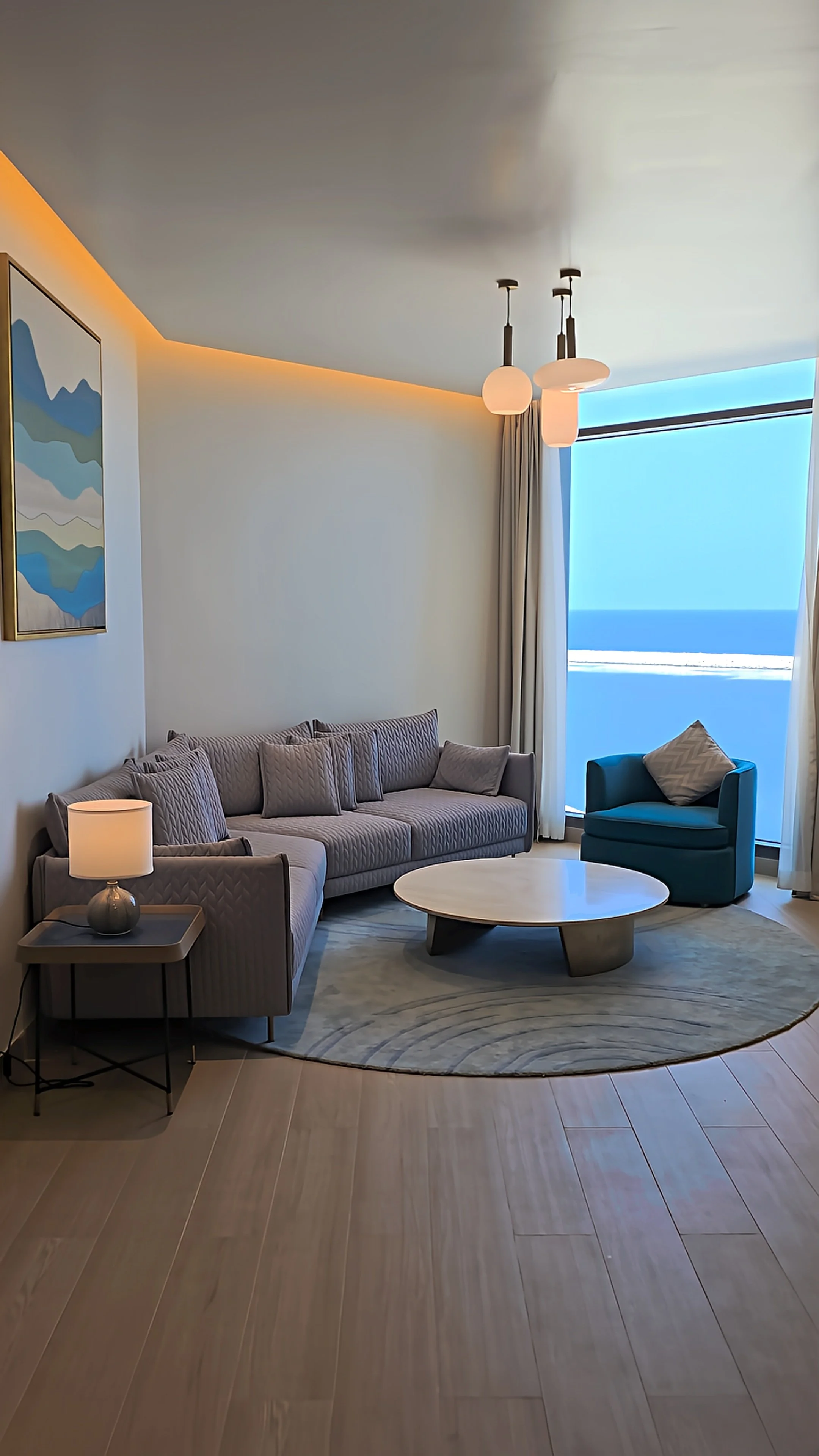 Contemporary hotel suite with a spacious sofa, blue armchair, elegant furnishings, and panoramic Arabian Sea views