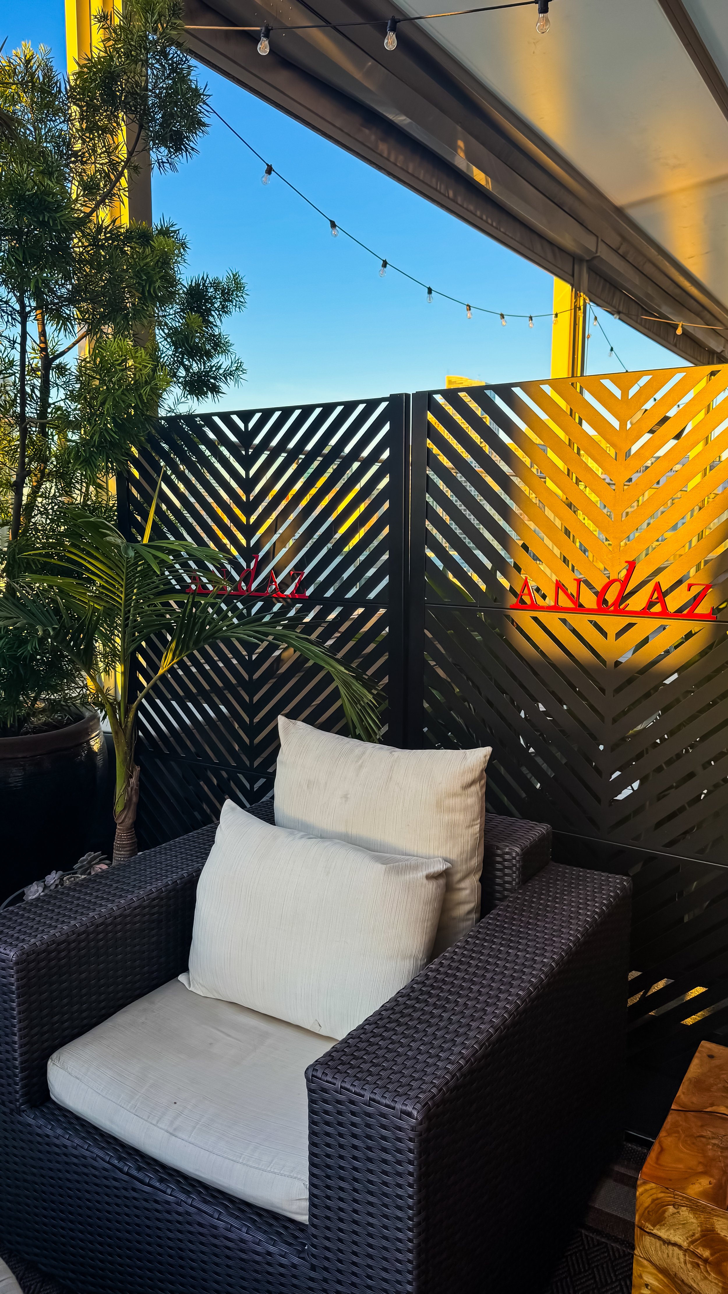 Stylish rooftop seating with patterned privacy screens, string lights, and palm accents at sunset, Andaz San Diego – San Diego, California.