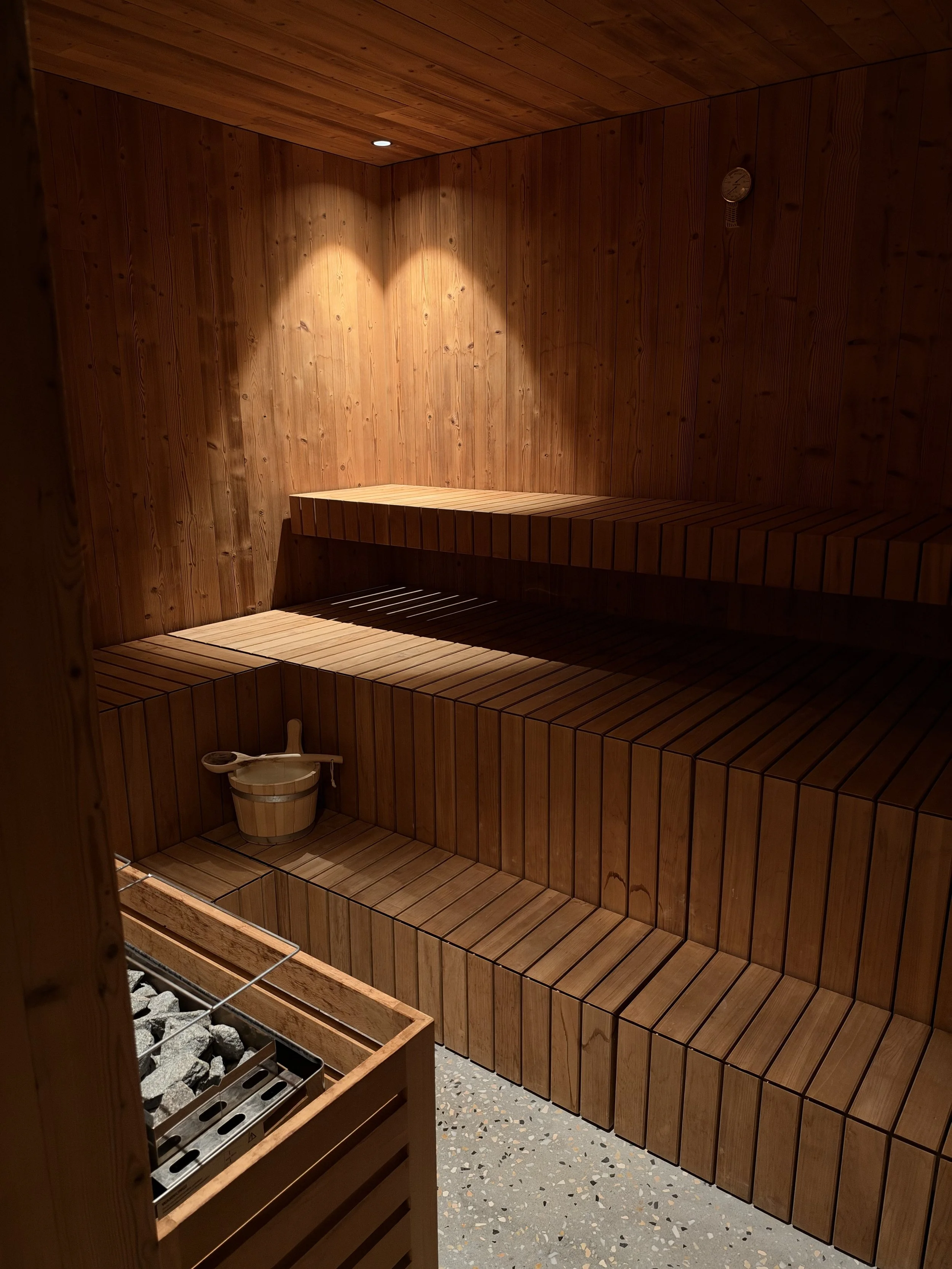 Traditional wooden sauna featuring tiered benches, warm ambient lighting, and a stone heater