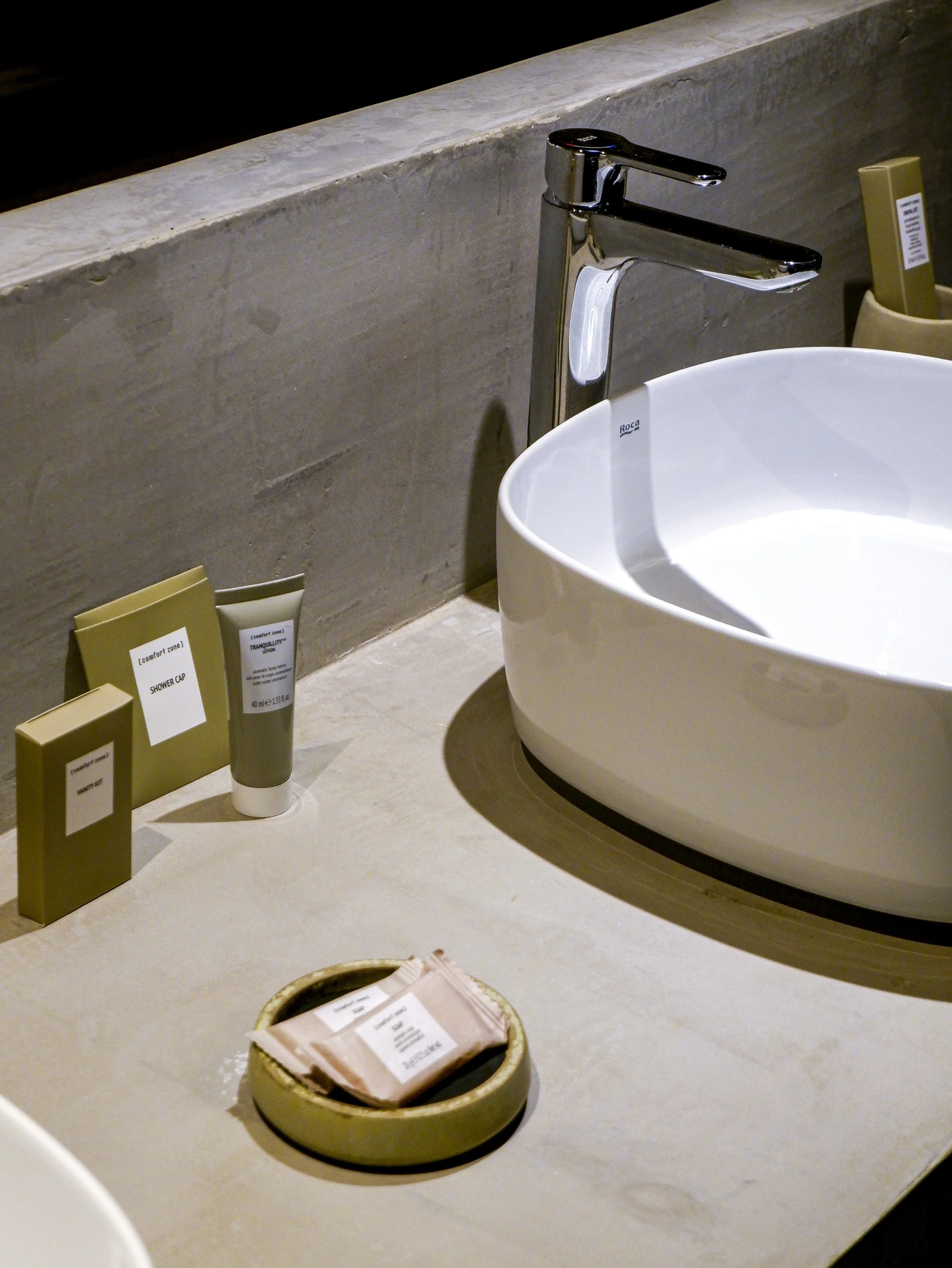 Close-up of minimalist stone vanity with white ceramic basin and curated bath amenities, highlighting refined simplicity and tactile natural materials, Land of Alandroal – Alandroal, Portugal.