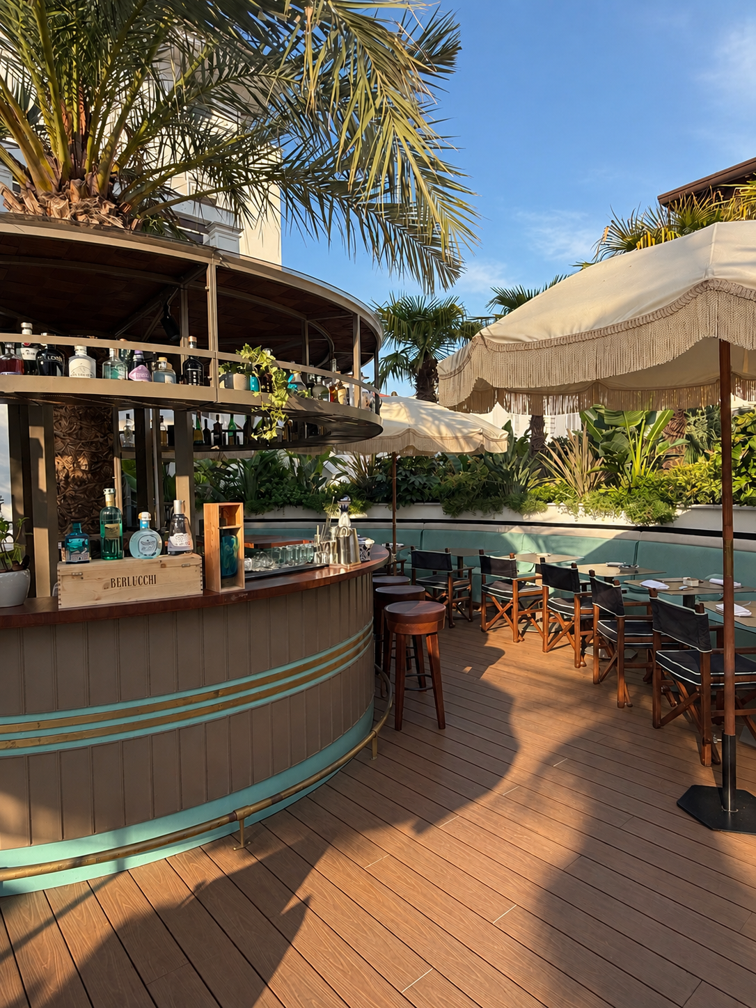 Outdoor garden bar with turquoise details, shaded seating, palm trees, and lush greenery