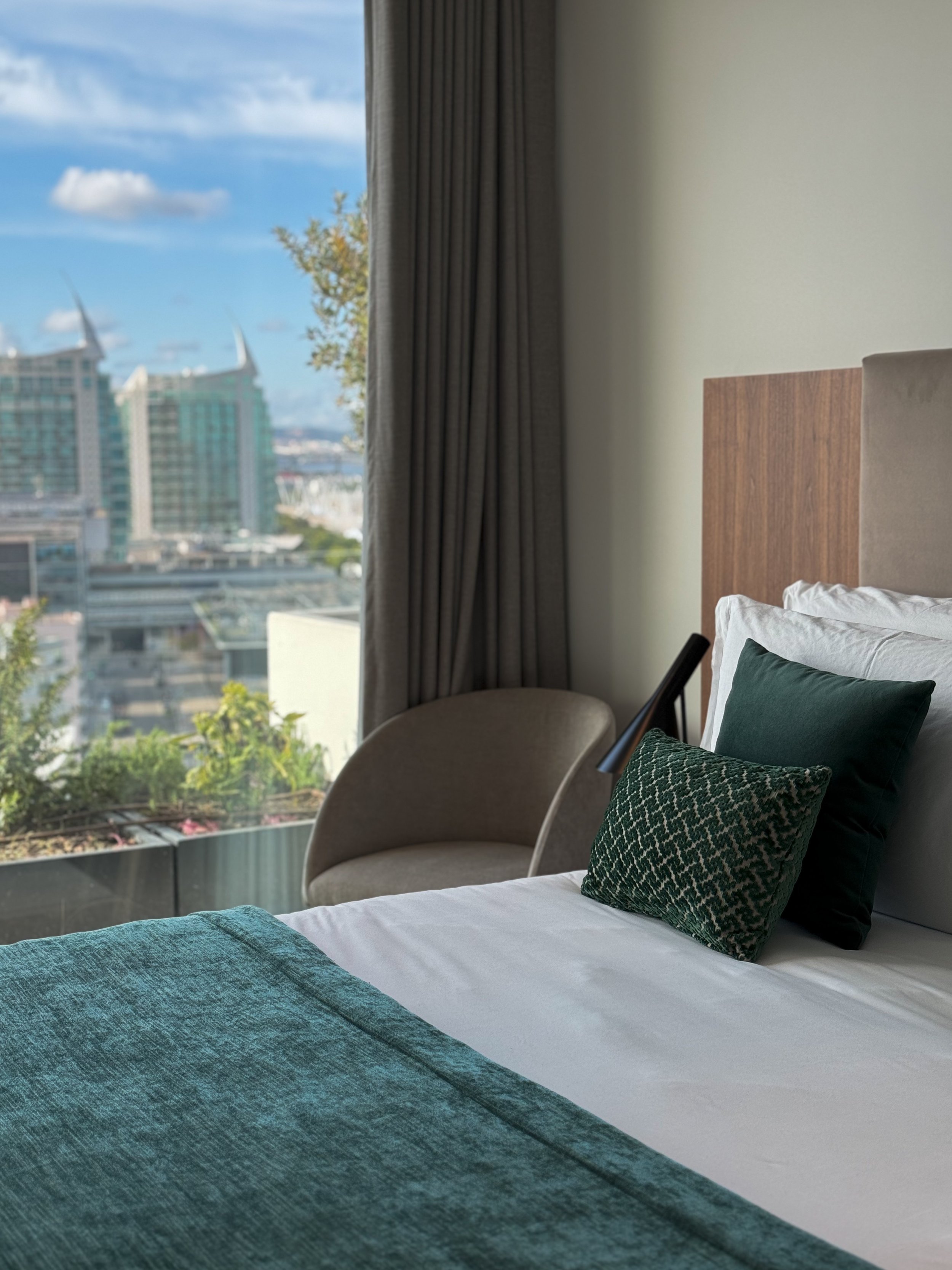 Stylish bedroom with city views, soft textiles, and modern furnishings overlooking Lisbon skyline, Martinhal Lisbon Oriente – Lisbon, Portugal.