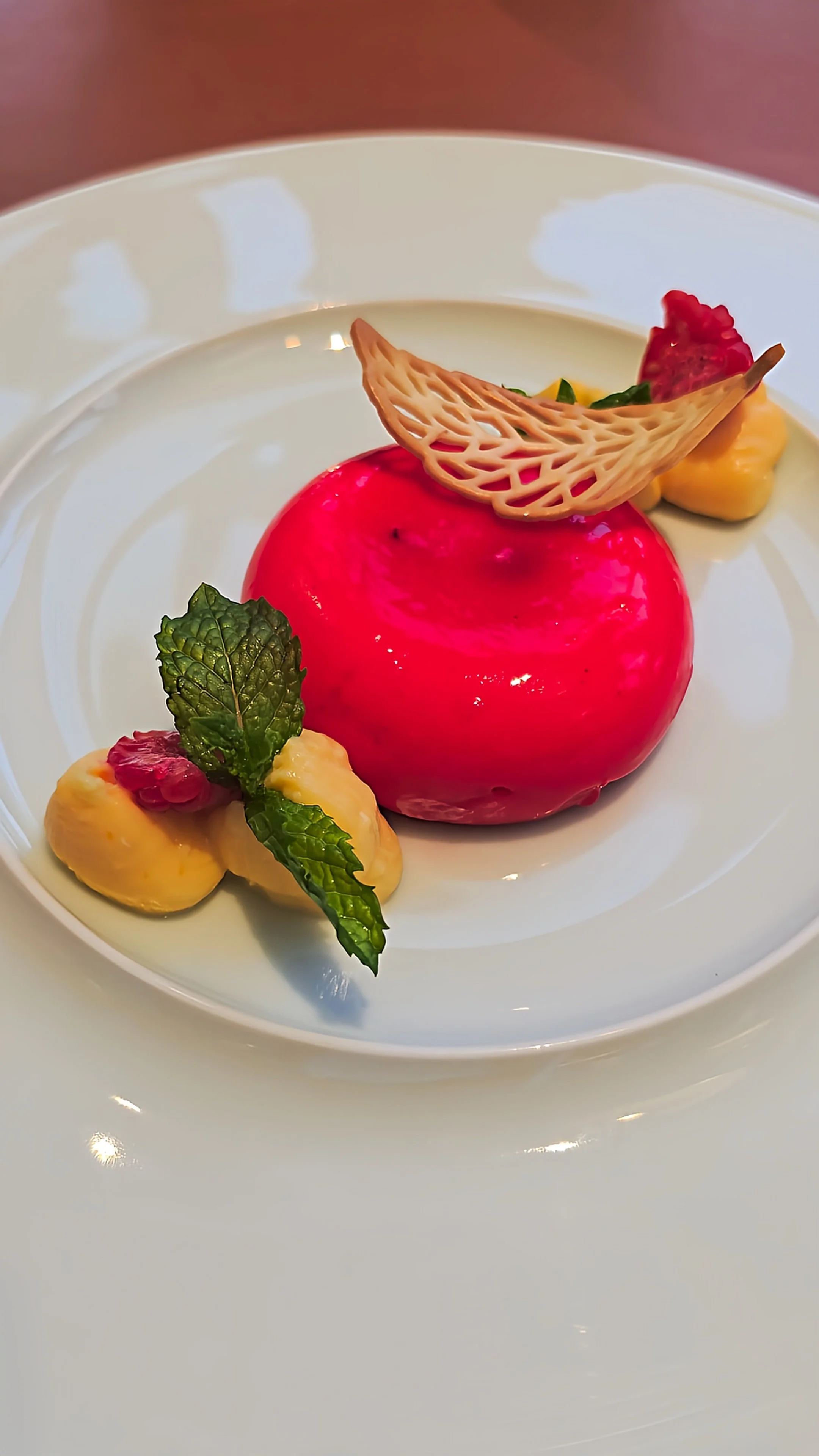 Elegant raspberry-glazed dessert decorated with fresh berries, mint leaves, delicate pastry, and cream