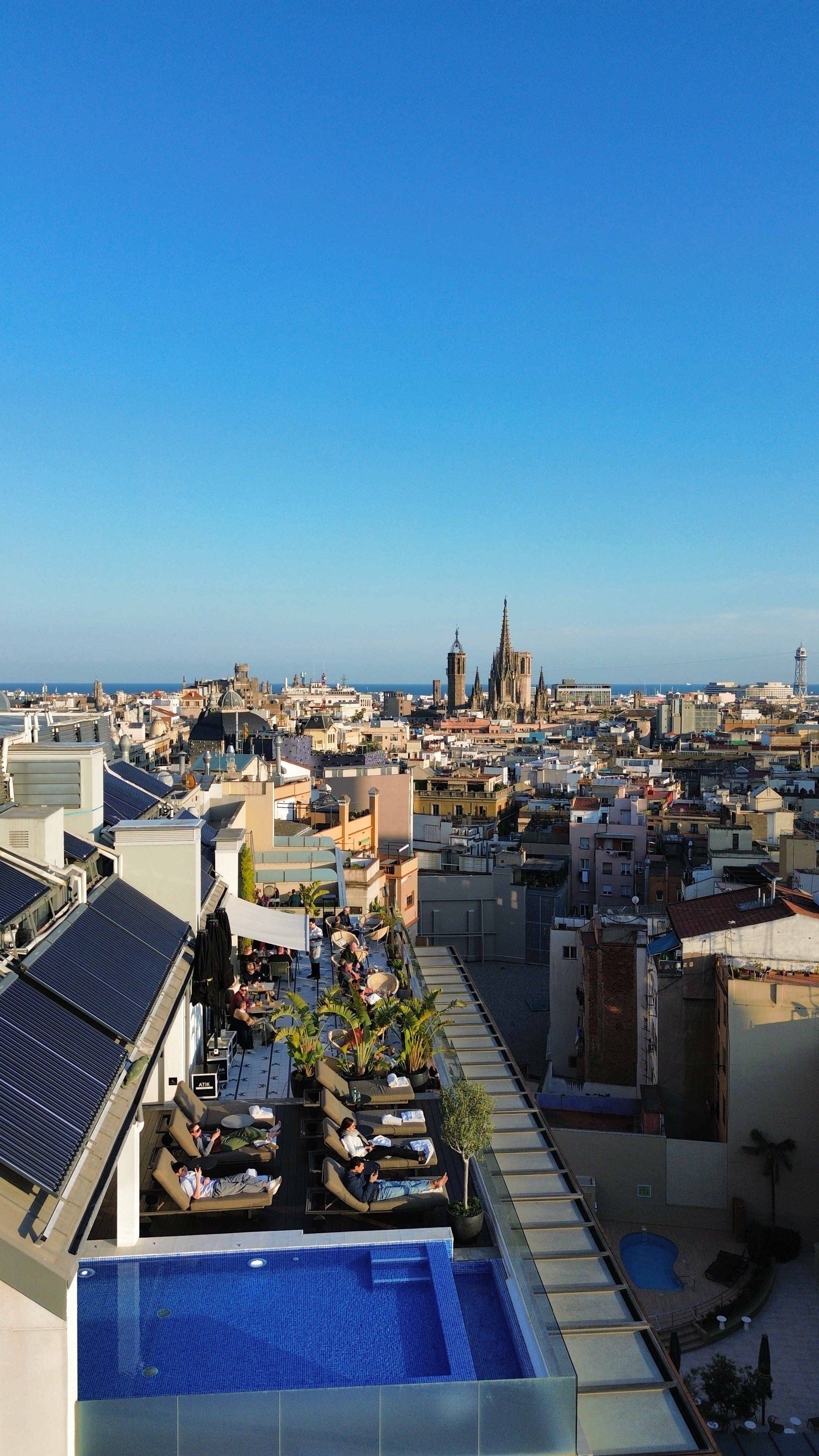 Rooftop pool and sun terrace with loungers overlooking historic city rooftops and skyline views, H10 Cubik Barcelona – Barcelona, Spain