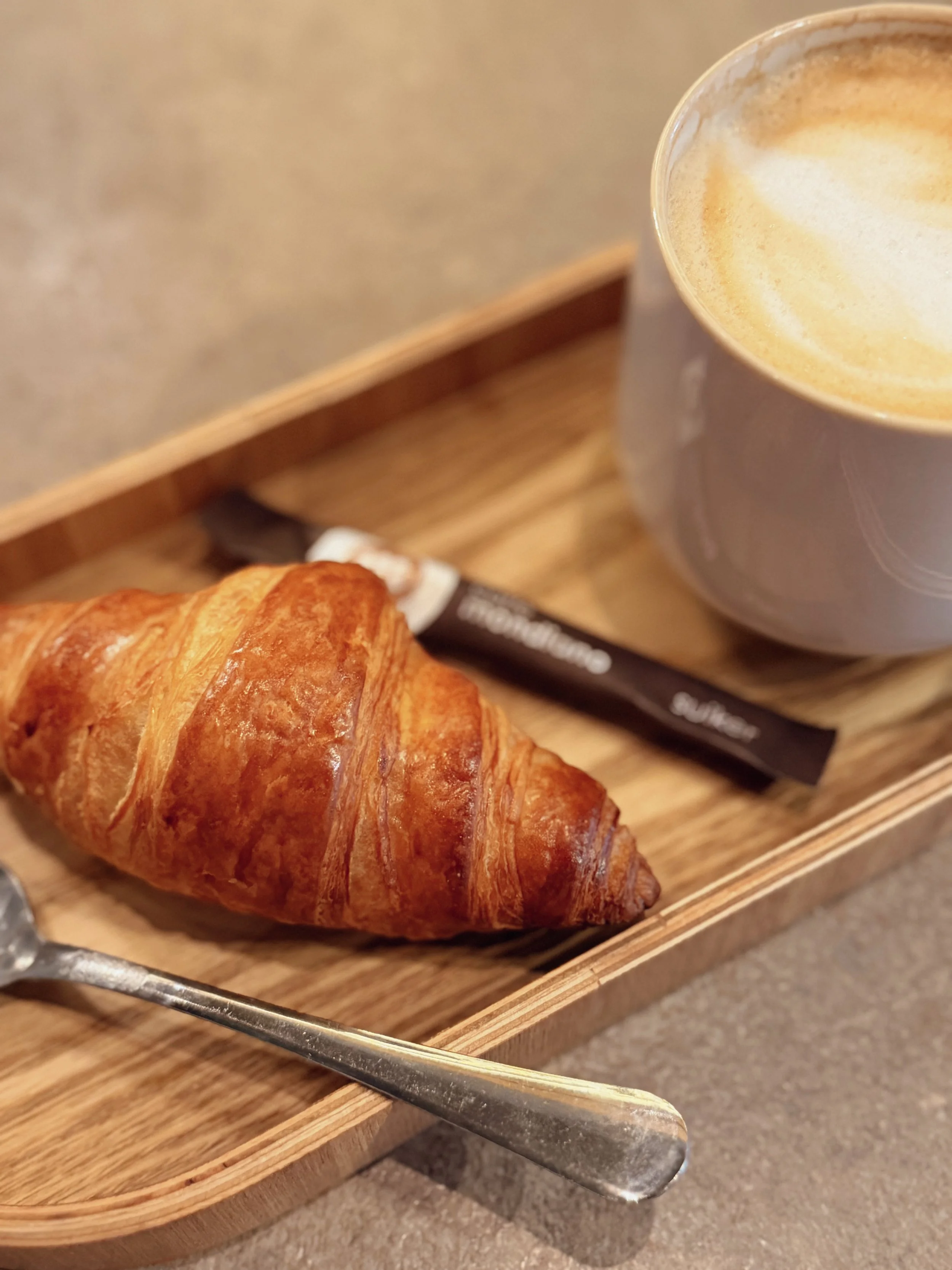 Fresh croissant and cappuccino served on a wooden breakfast tray