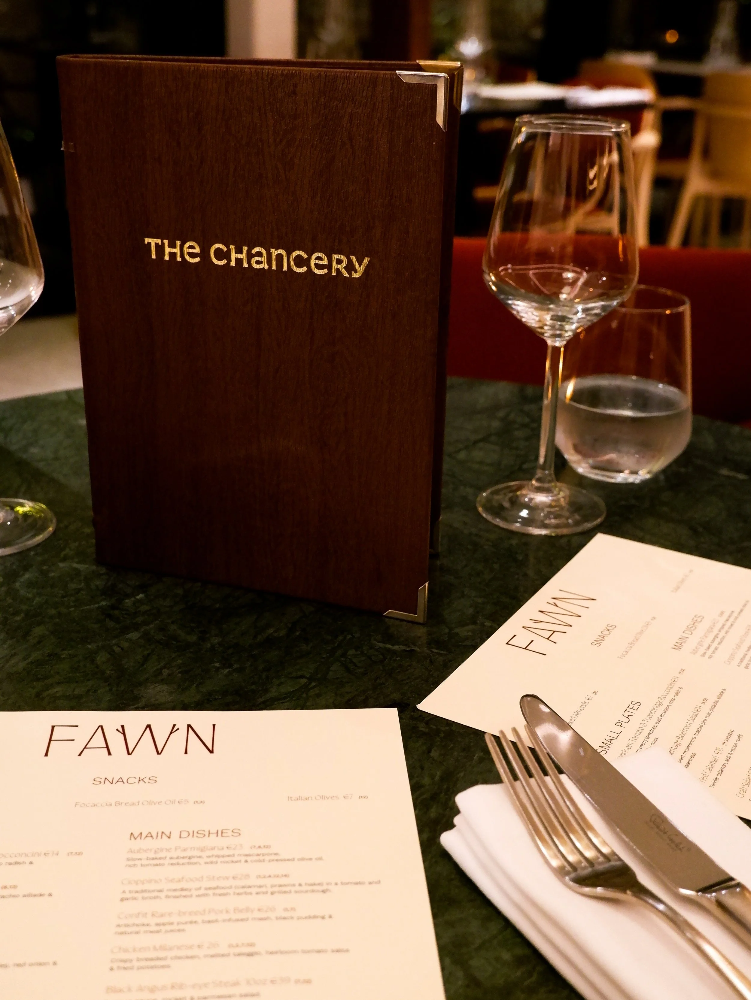 Elegant restaurant table setting with wooden menus, wine glasses, and polished cutlery on a green marble table