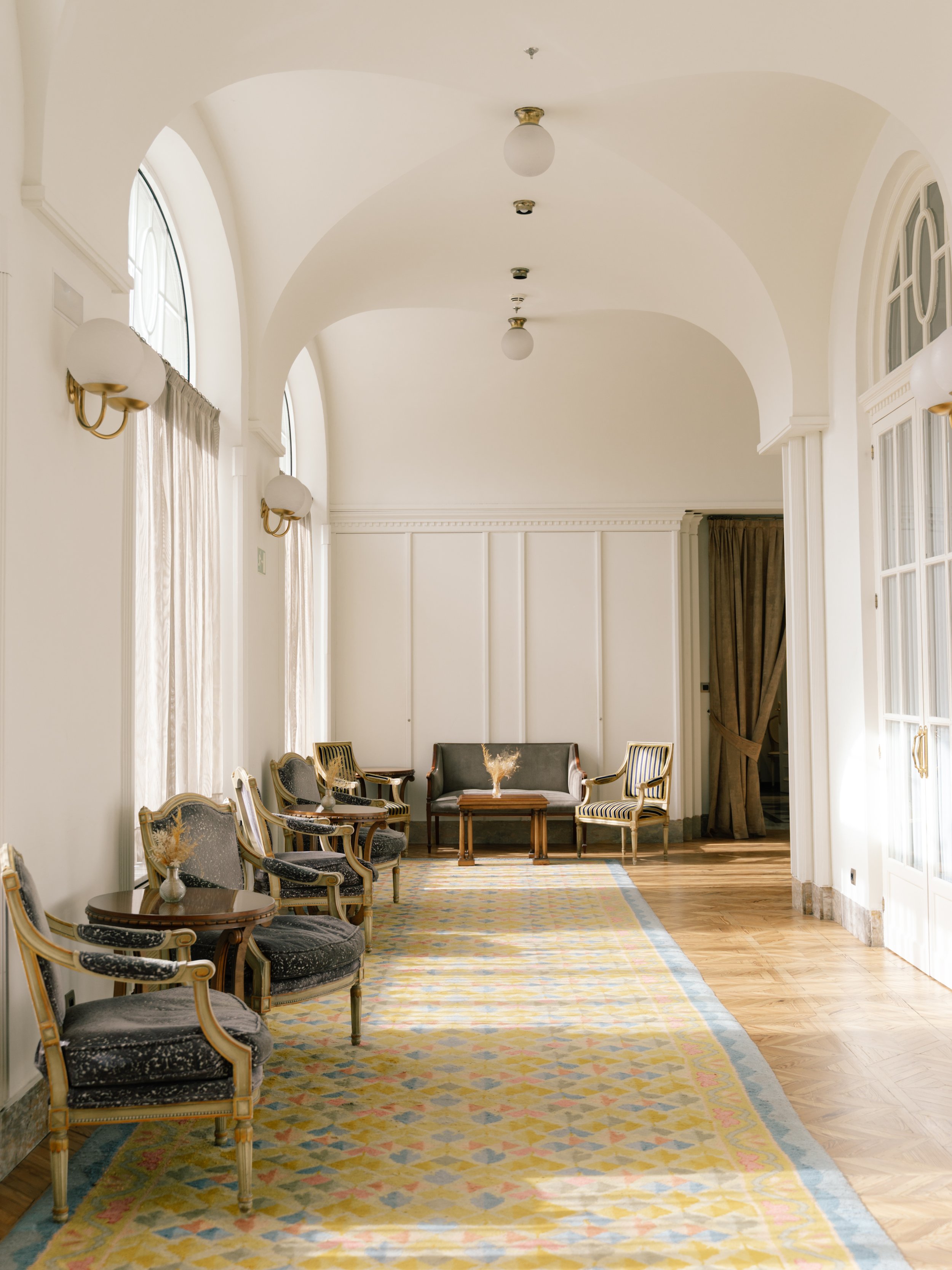 Sunlit corridor with arched windows and classic lounge seating